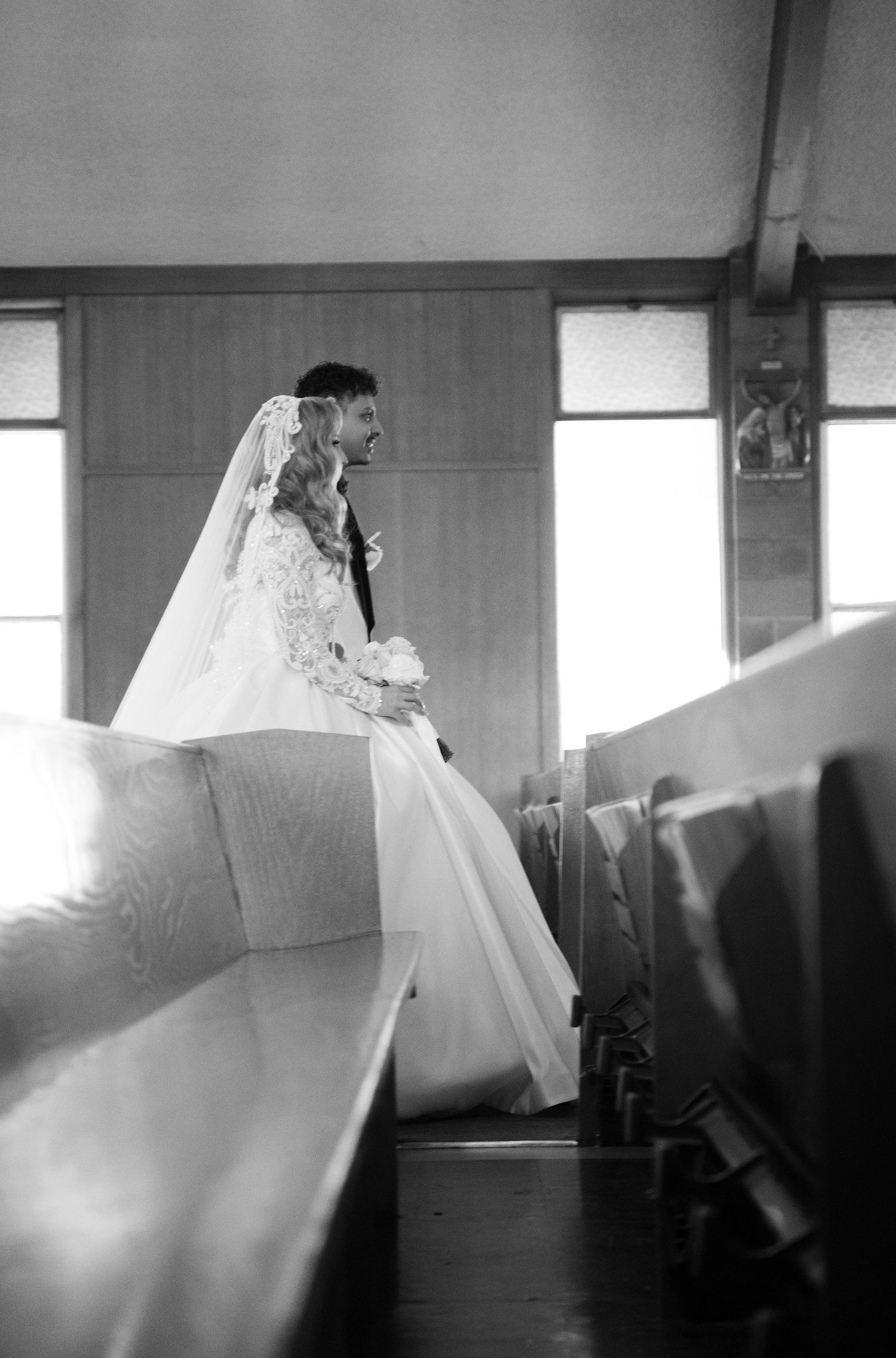Black and white wedding photo showing bride in flowing dress near church windows.