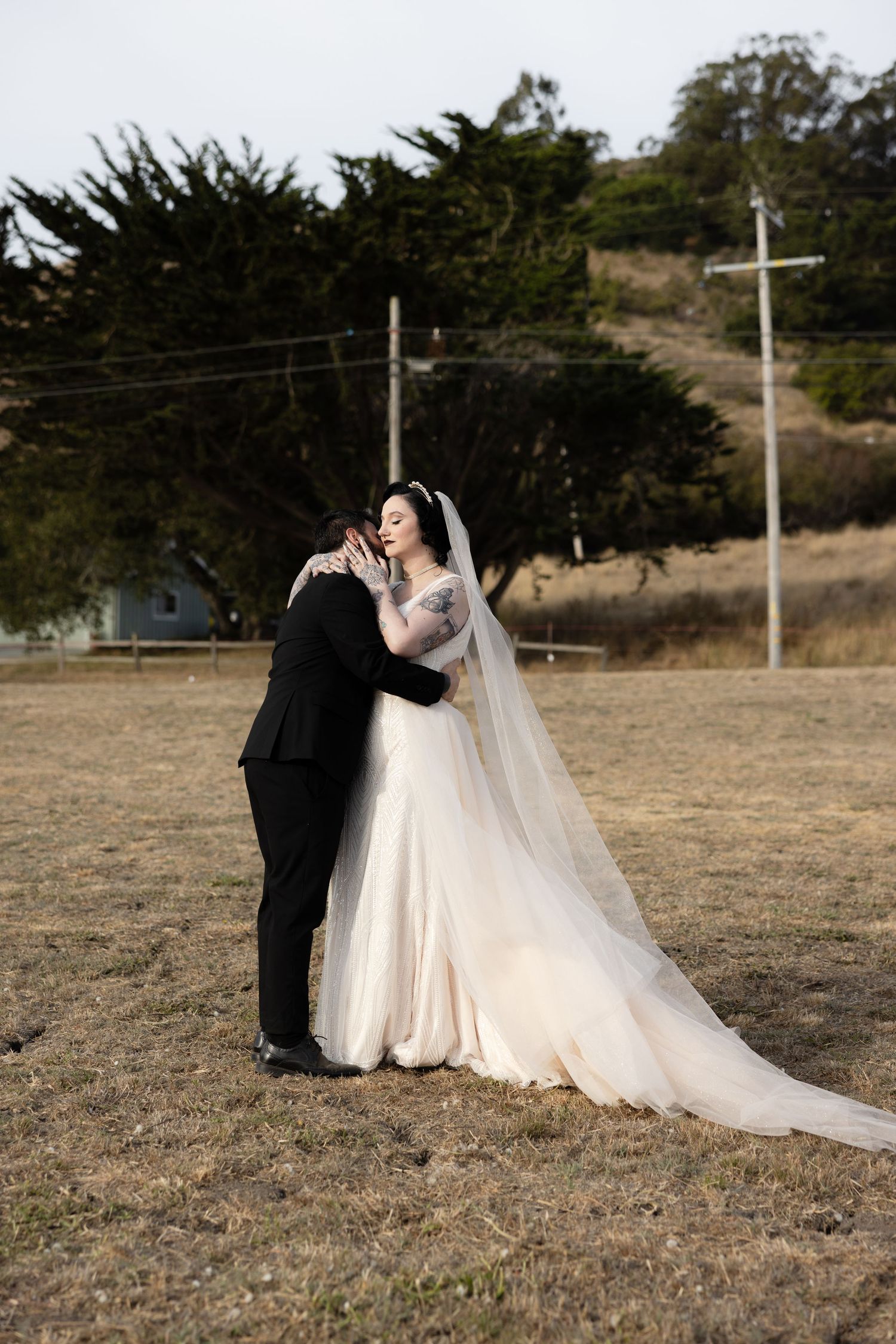 Romantic wedding portrait in desert setting with power lines and cypress trees in background.
