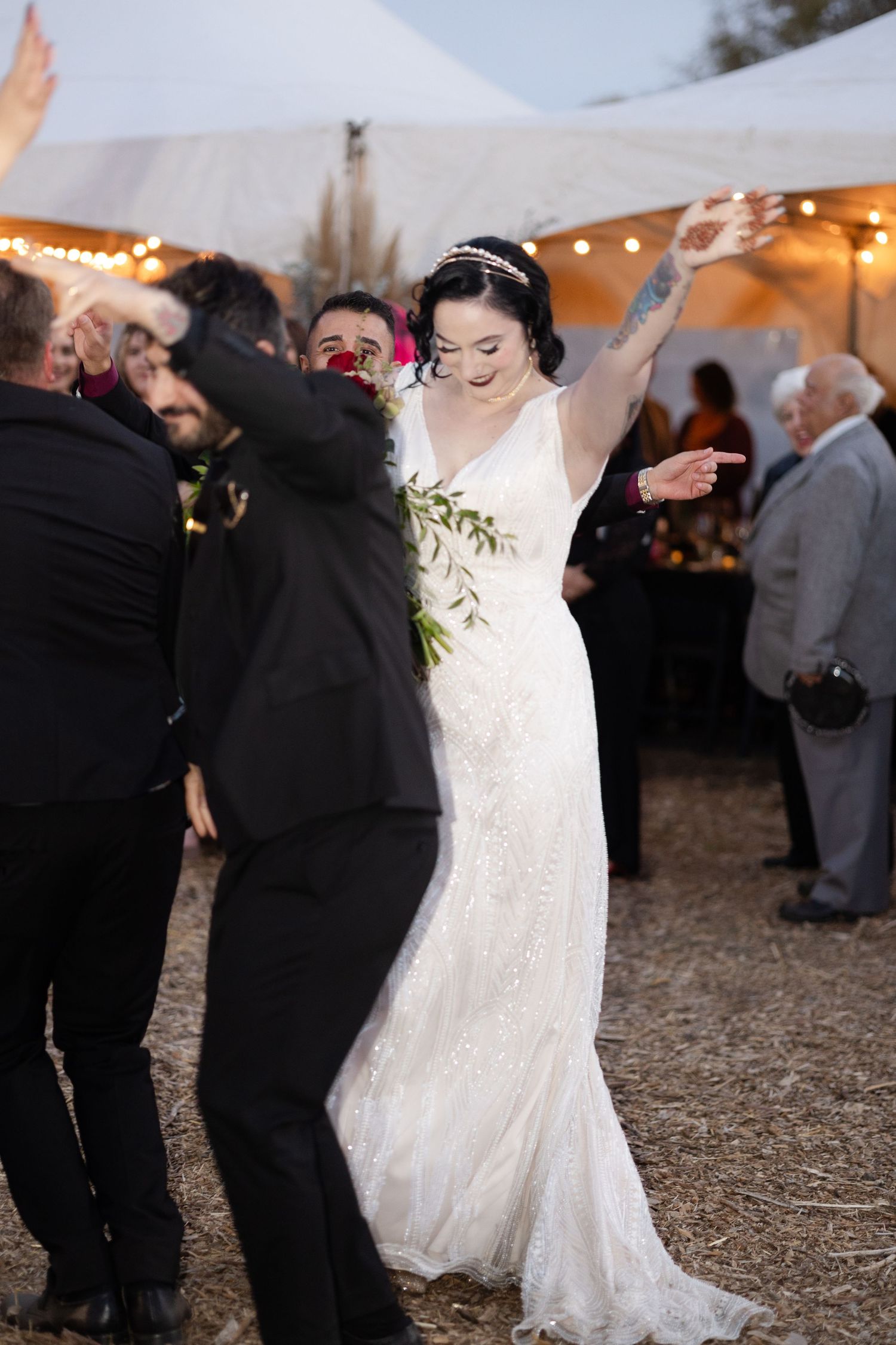Wedding guests dance and celebrate under a white tent with string lights.