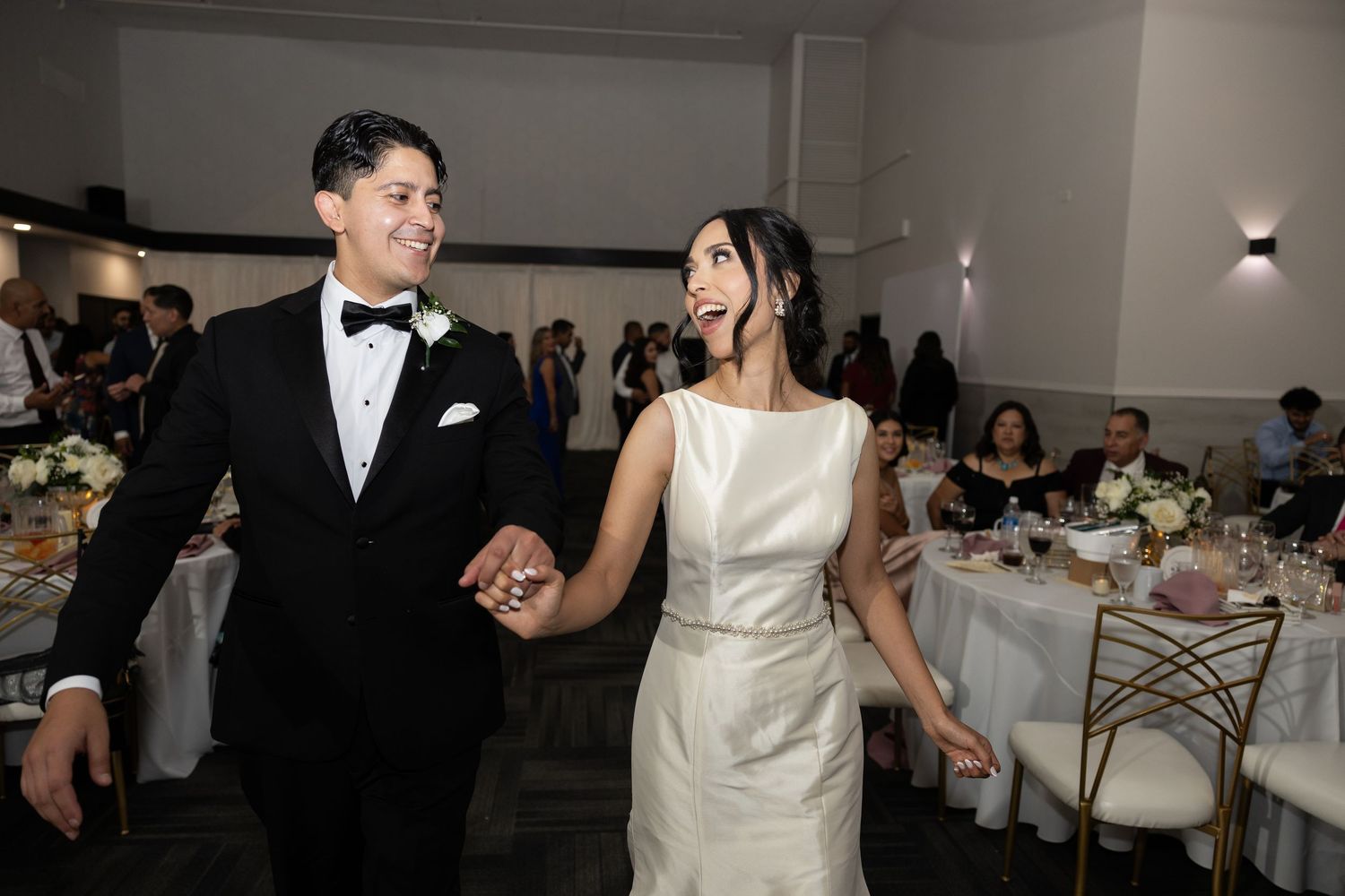 Elegant wedding reception with guests dancing in formal attire under indoor lighting.