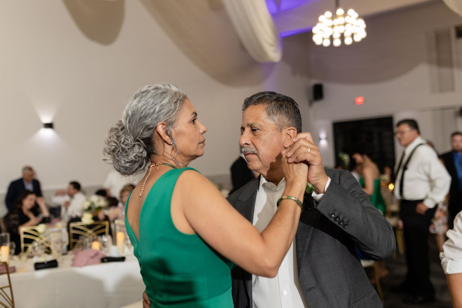 Couples share intimate dances under crystal chandeliers at an elegant wedding venue.
