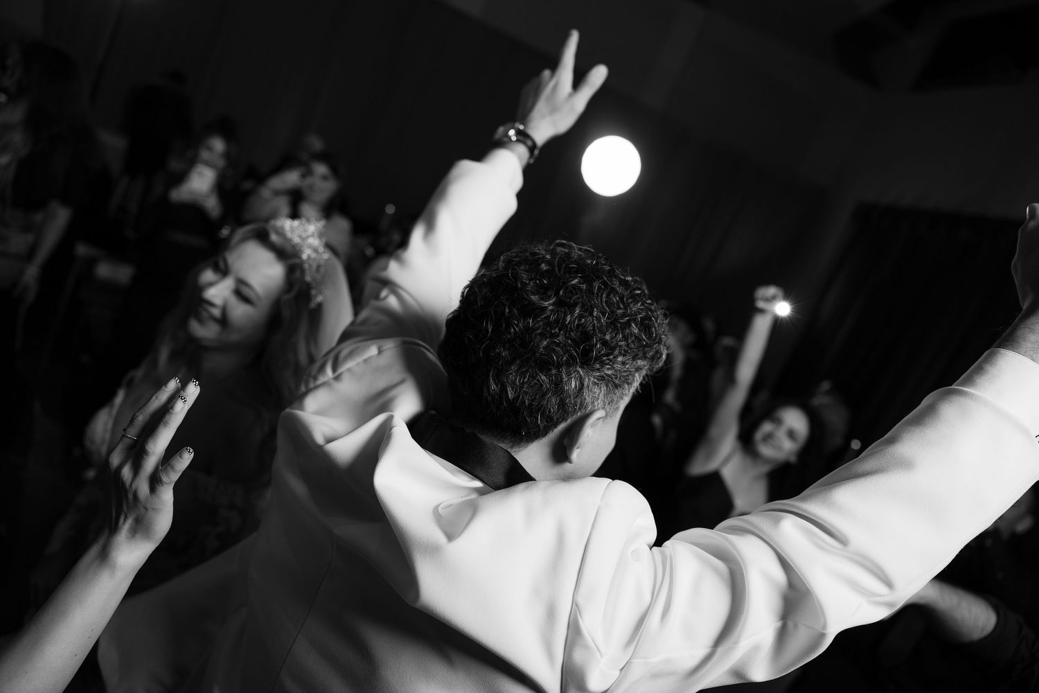 Black and white photo of wedding guests dancing energetically at a reception.