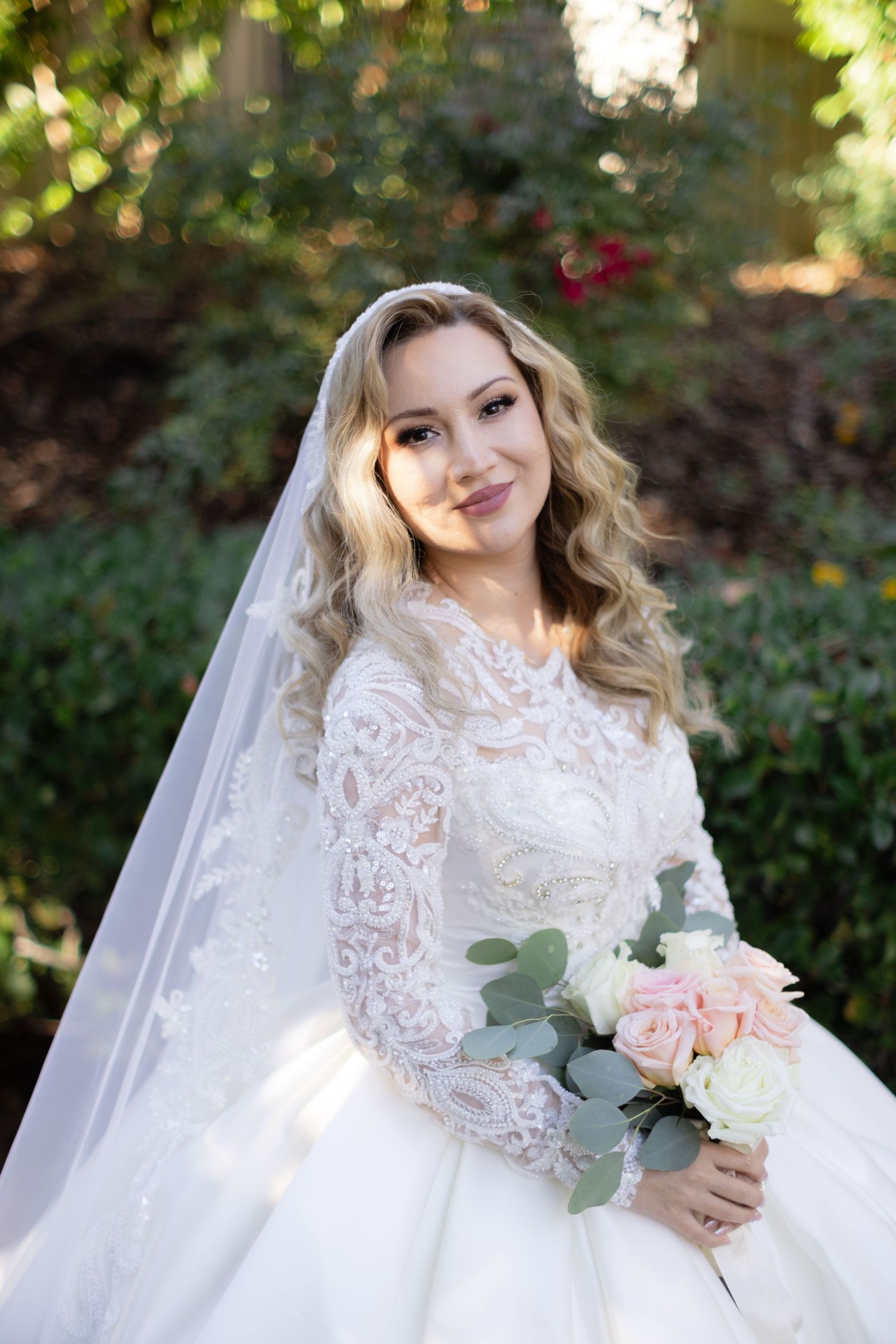 Romantic bridal portrait in garden setting with pink roses and eucalyptus bouquet.