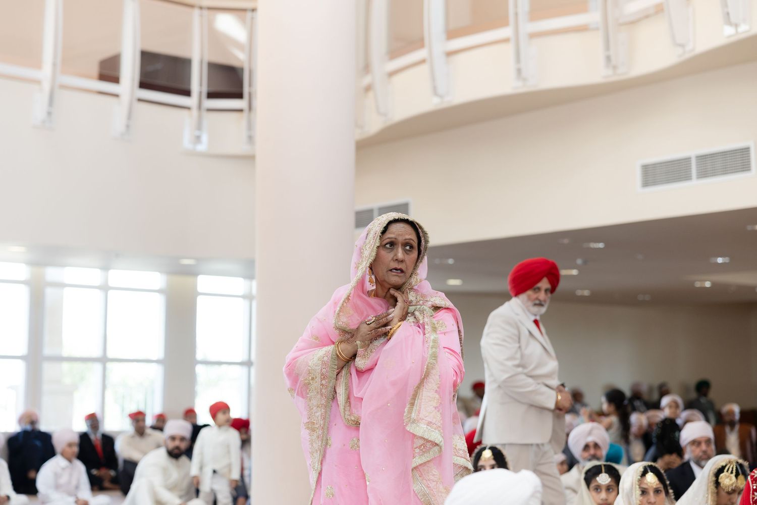 Wedding guests in traditional attire gather in a modern indoor venue with balcony.