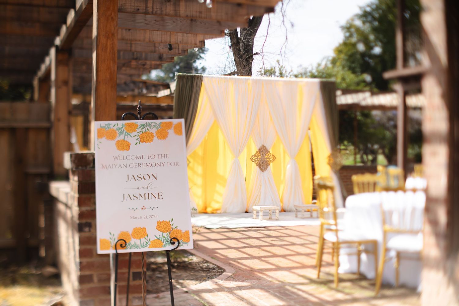 A wedding ceremony setup with a yellow backdrop and white chairs in an outdoor brick courtyard setting.