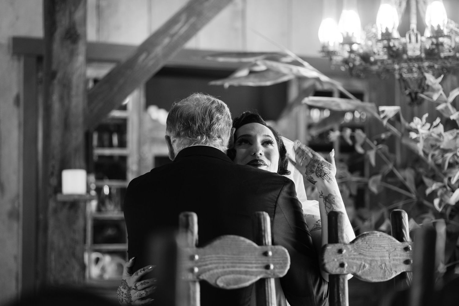Black and white photo of an intimate moment in a rustic wooden venue with chairs.