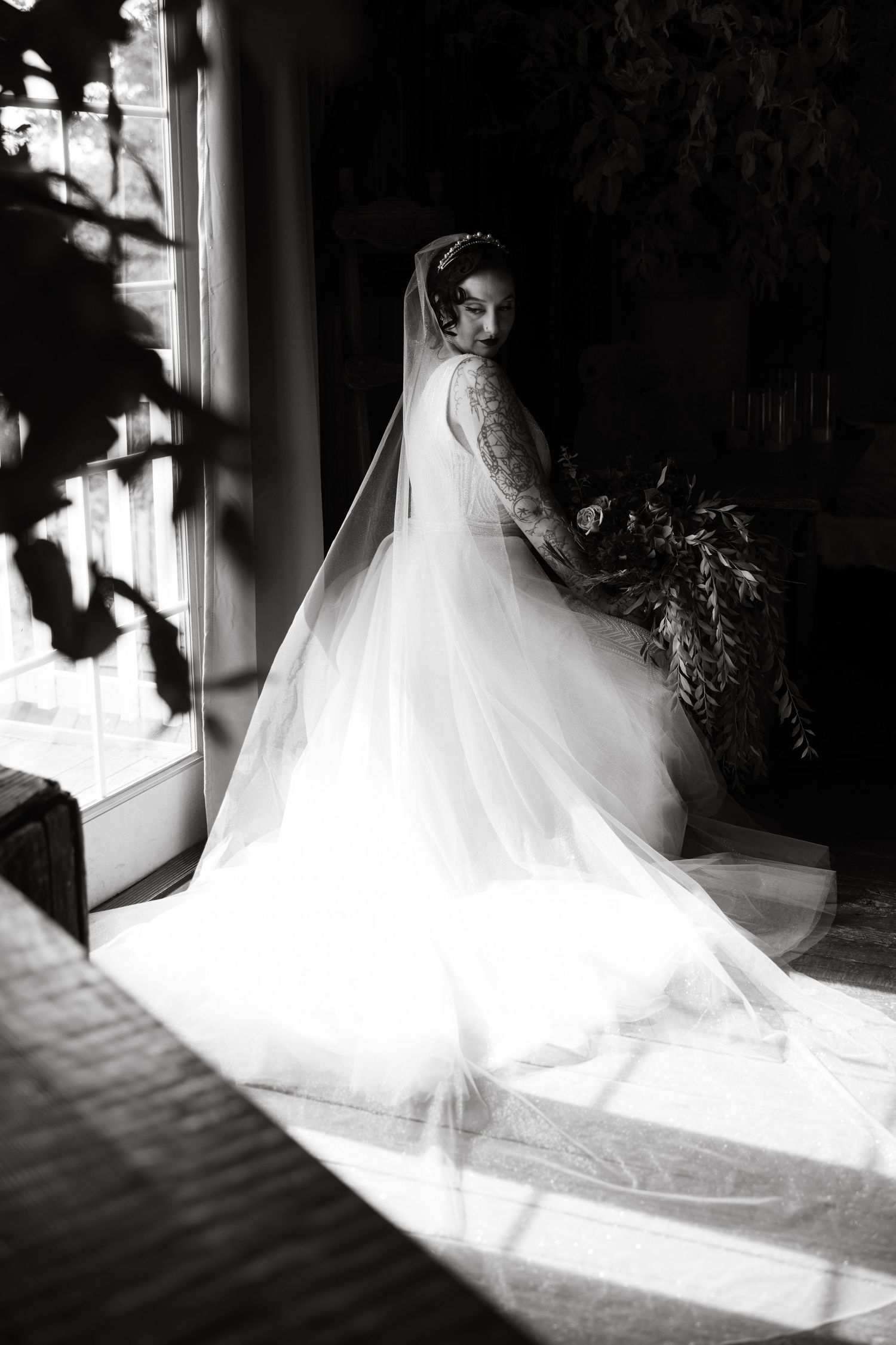 A flowing white wedding dress train illuminated by natural window light in a dark room.