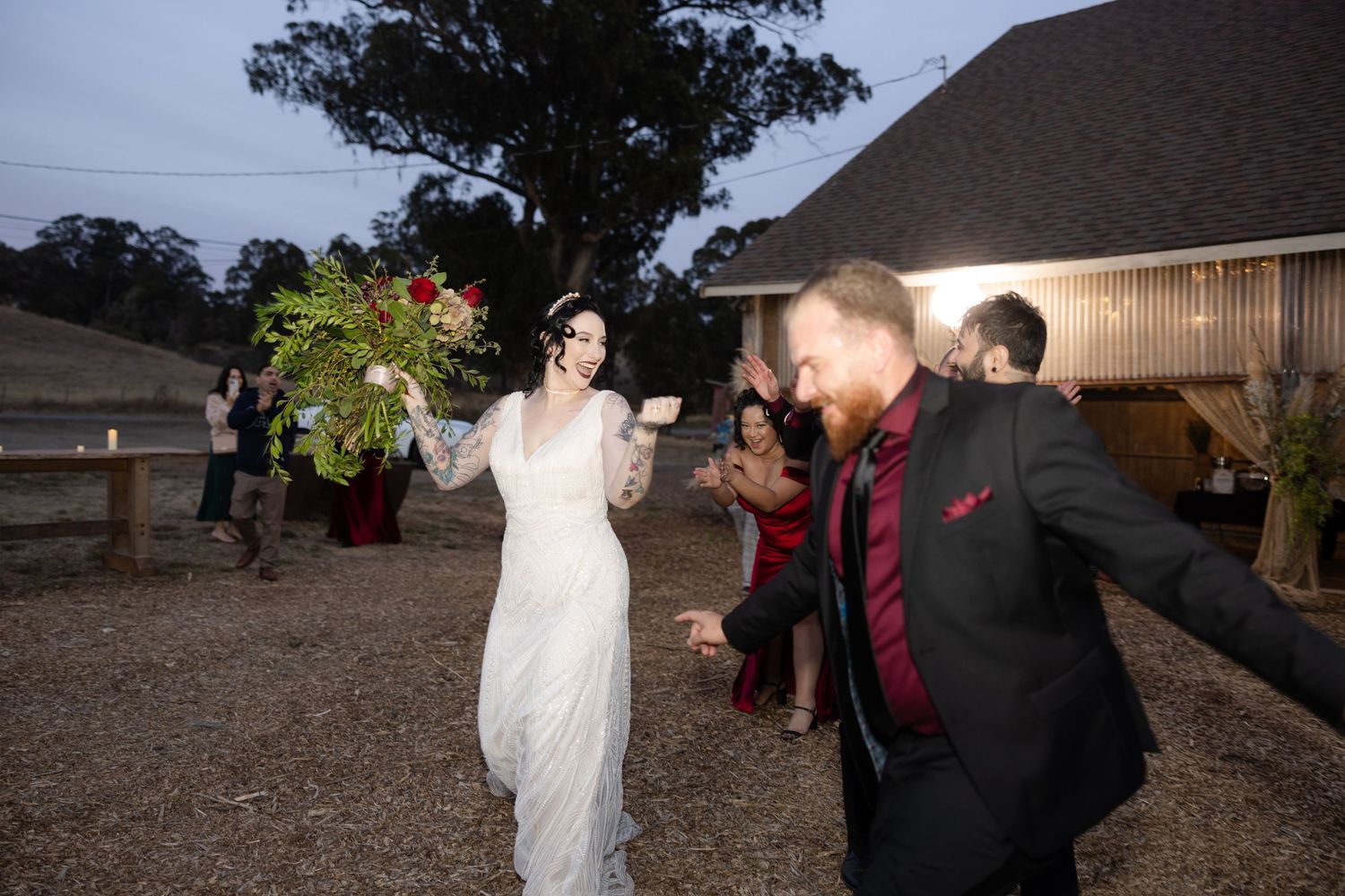 Wedding party dancing and celebrating outside rustic venue at night.