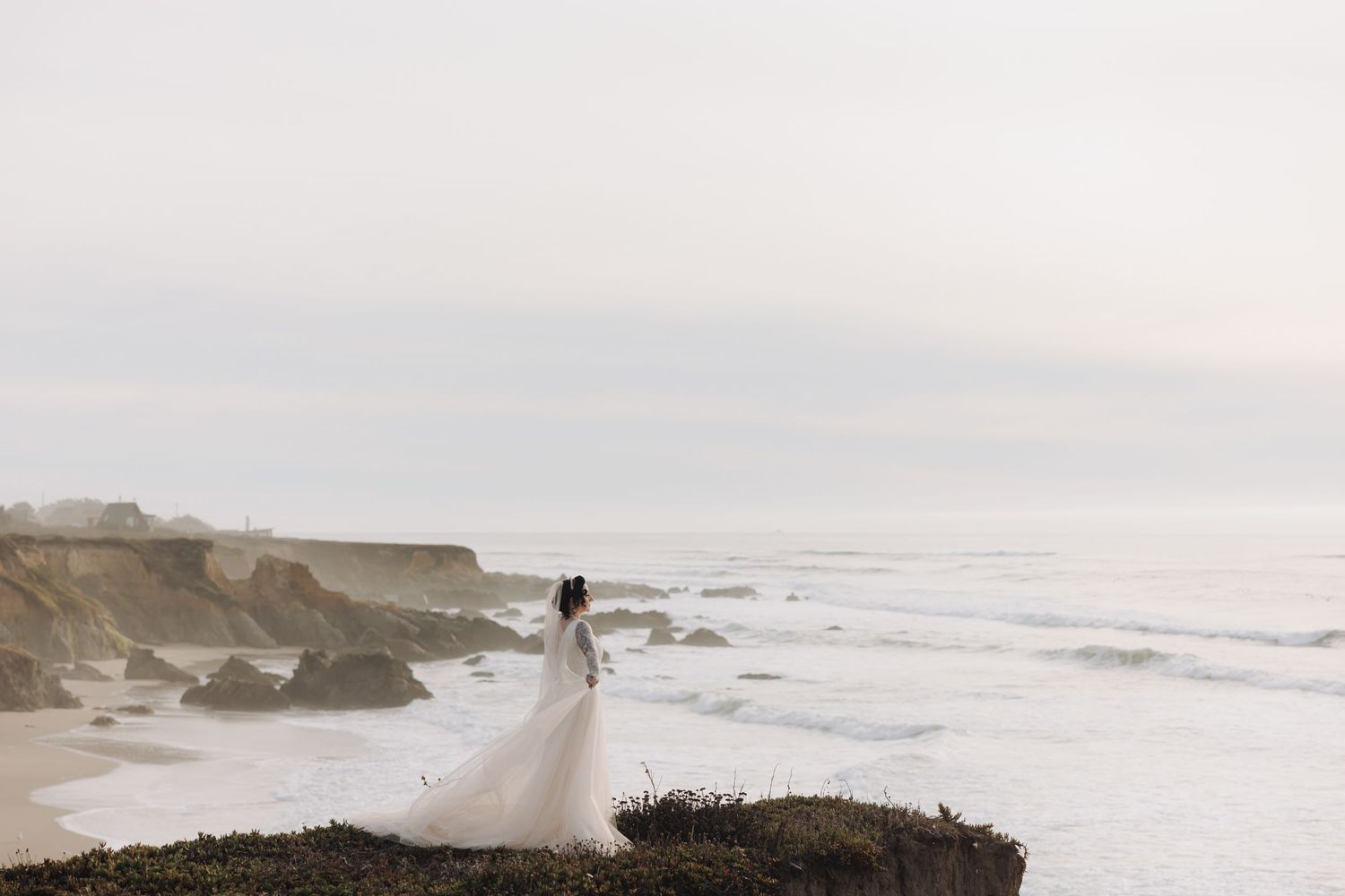 An ethereal wedding photo captured on dramatic coastal cliffs overlooking a misty ocean.