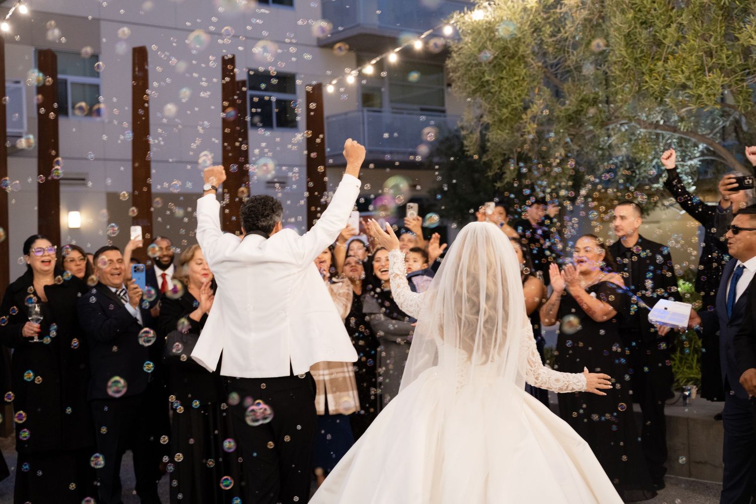 Elegant bride in white ballgown twirls with groom during wedding dance under string lights.