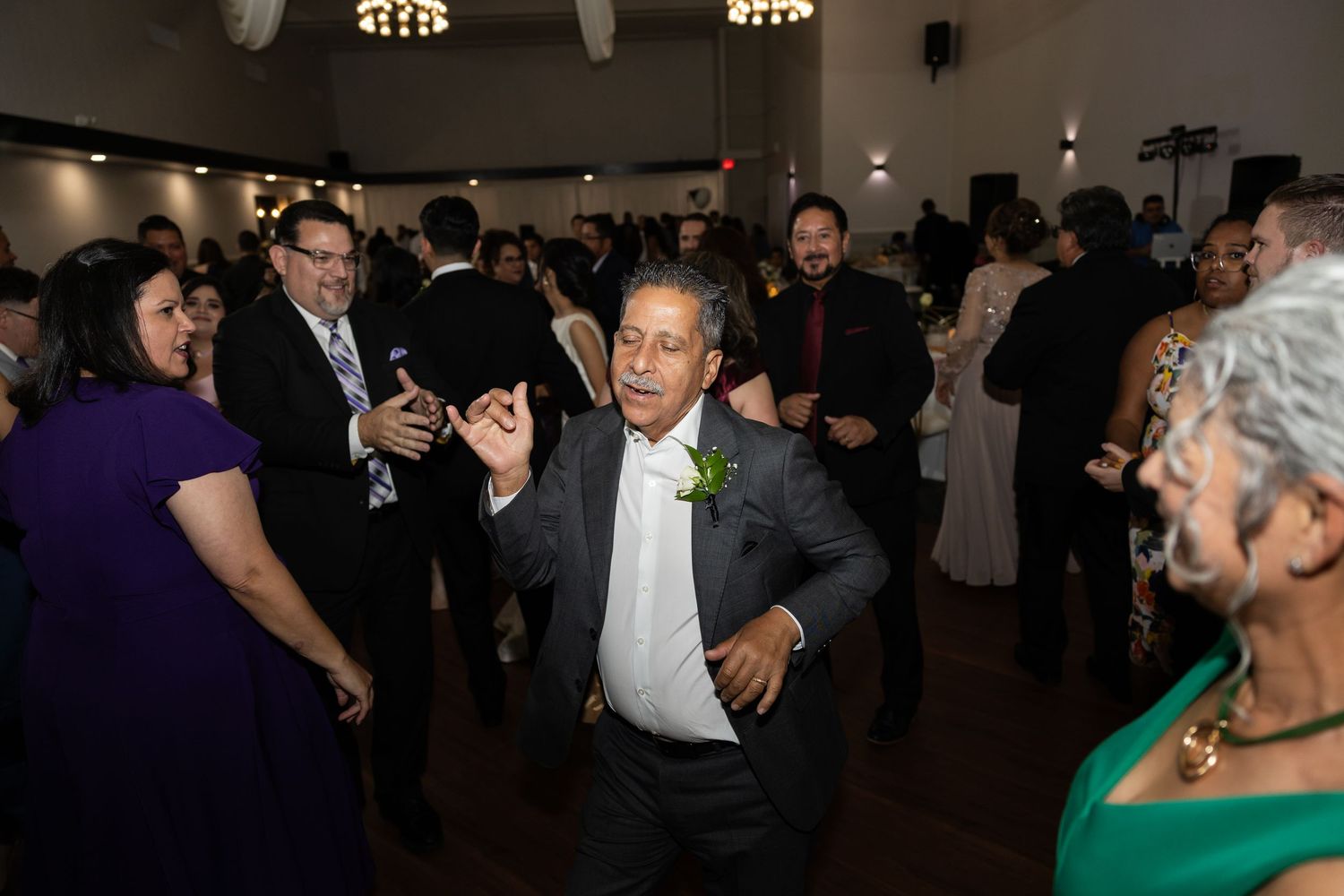 Wedding reception guests dancing and celebrating on a dimly lit dance floor.