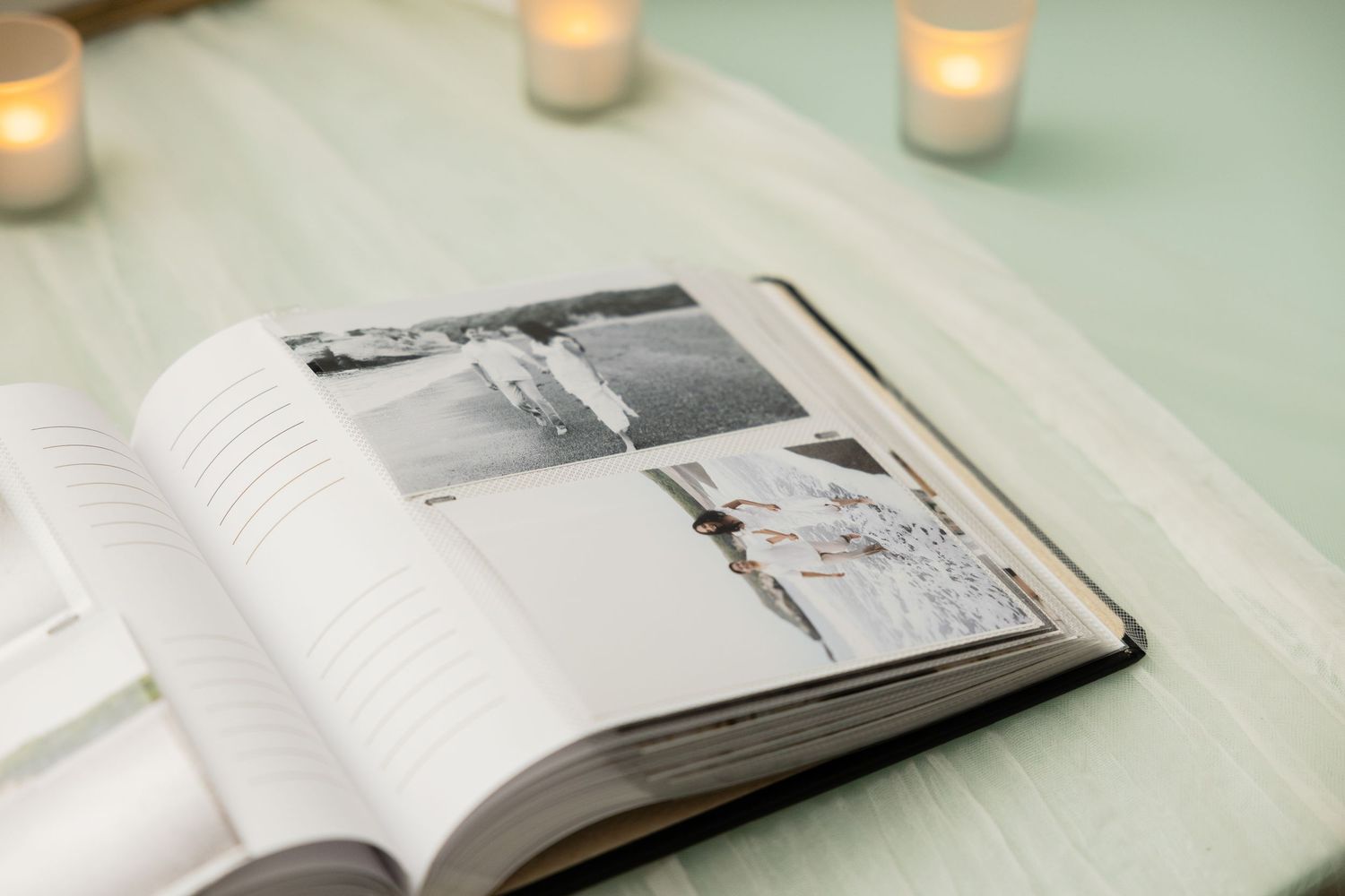 Open wedding photo album displayed with soft candlelight on mint green surface.