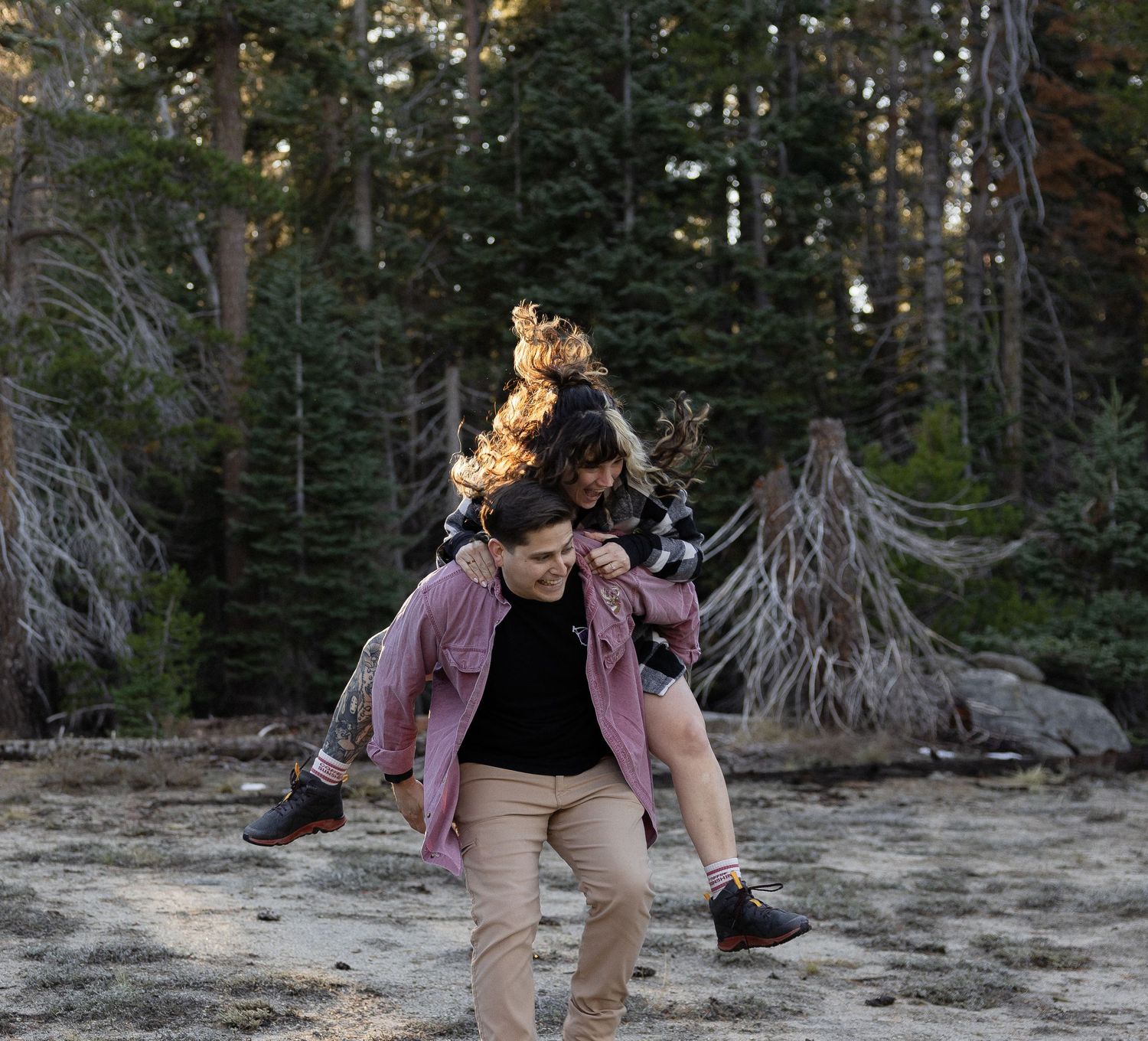 Couple sharing intimate moment on rocky terrain in forest setting.