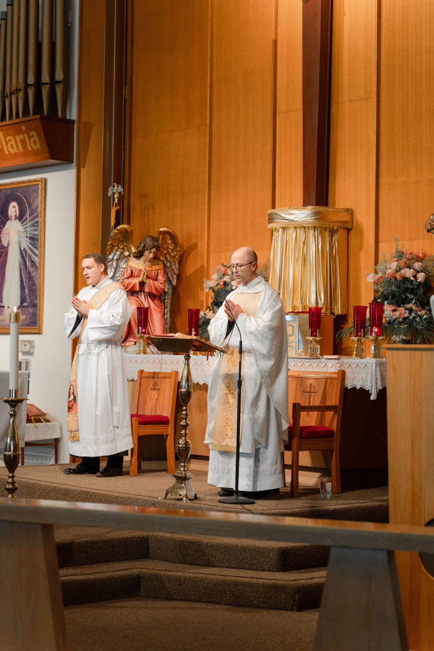 Clergy members in white robes conduct a religious ceremony at the altar of a church.