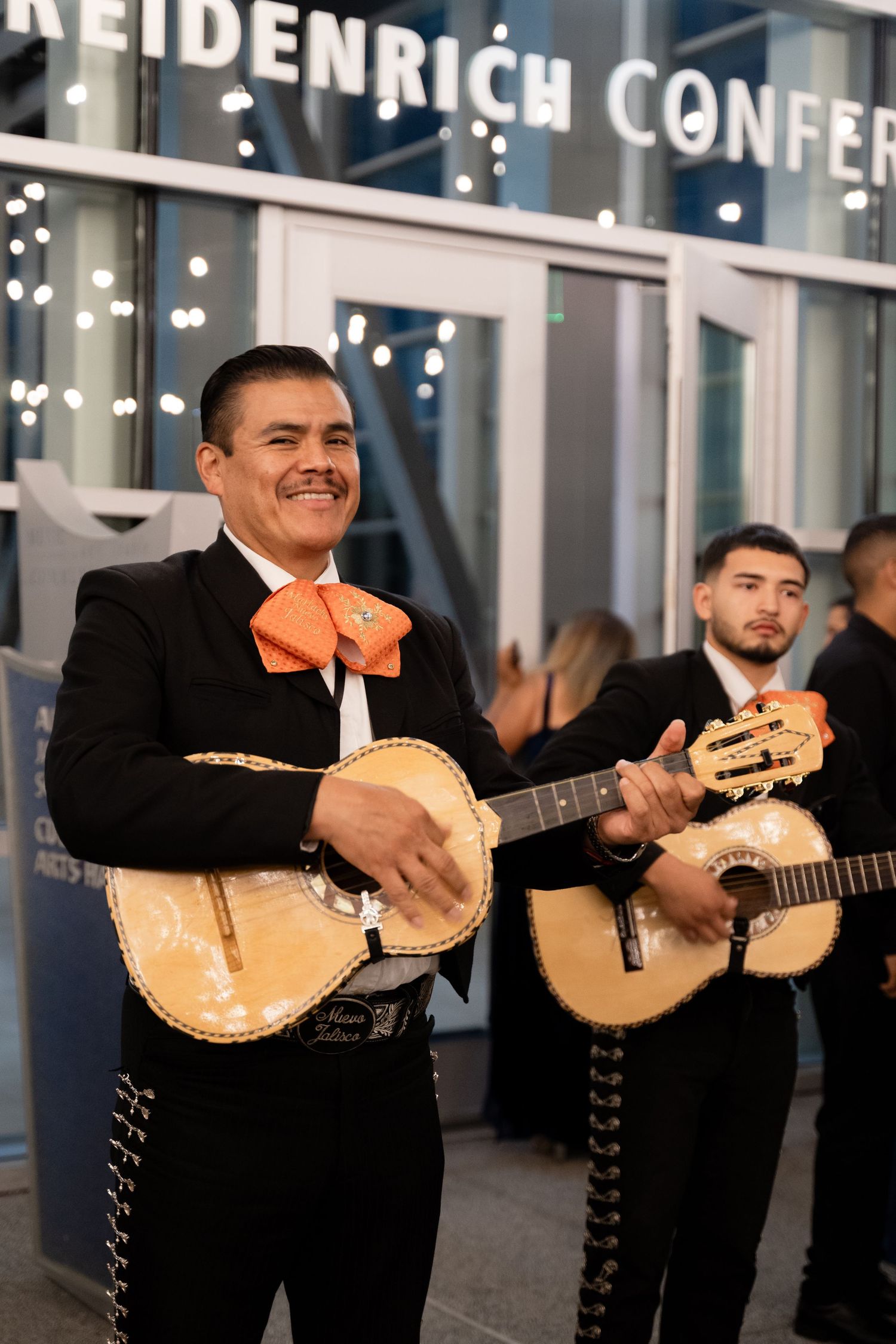 Musicians in black suits perform with traditional mariachi instruments at a wedding reception.