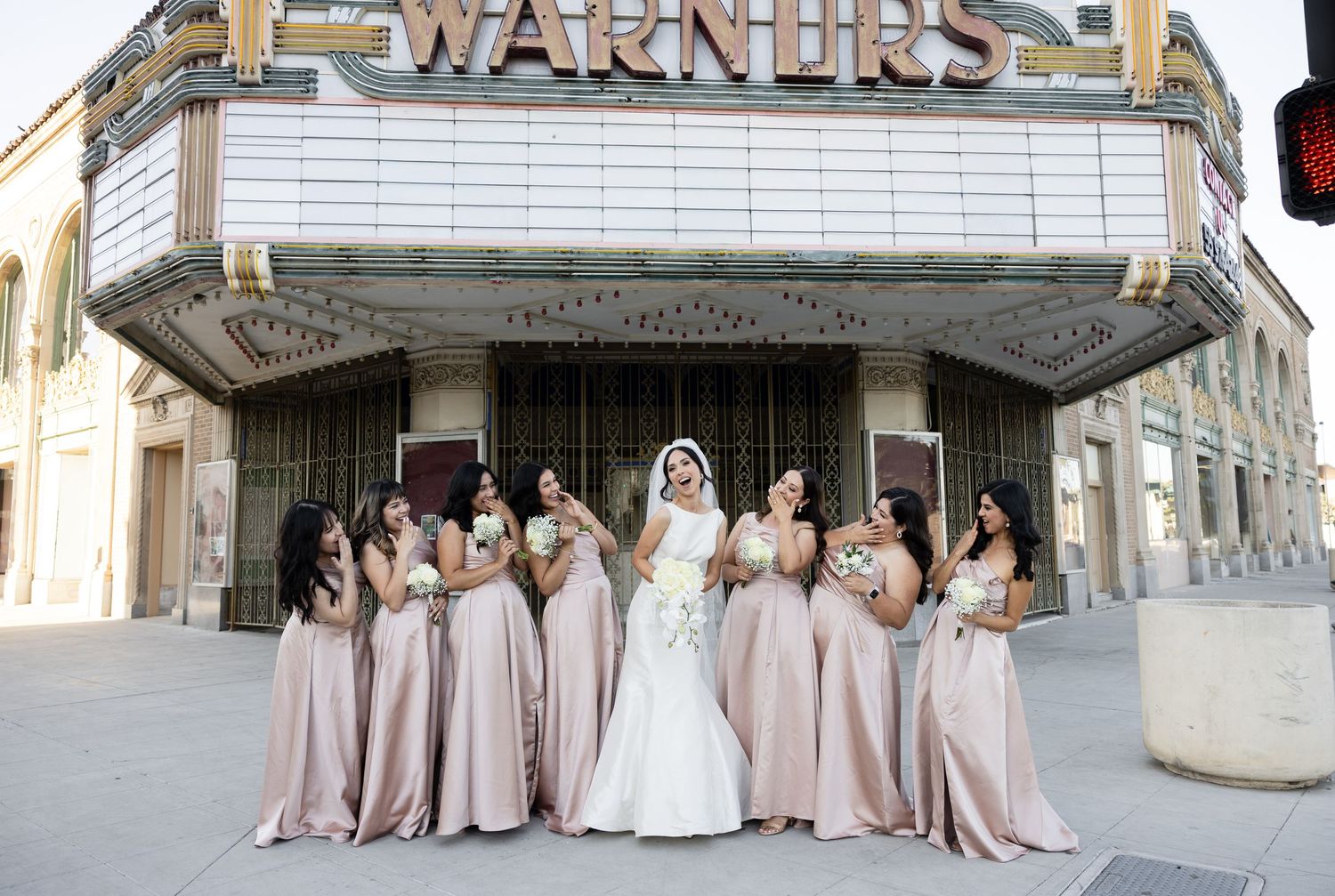 Wedding party poses in formal attire outside historic stone building with Warner's sign.