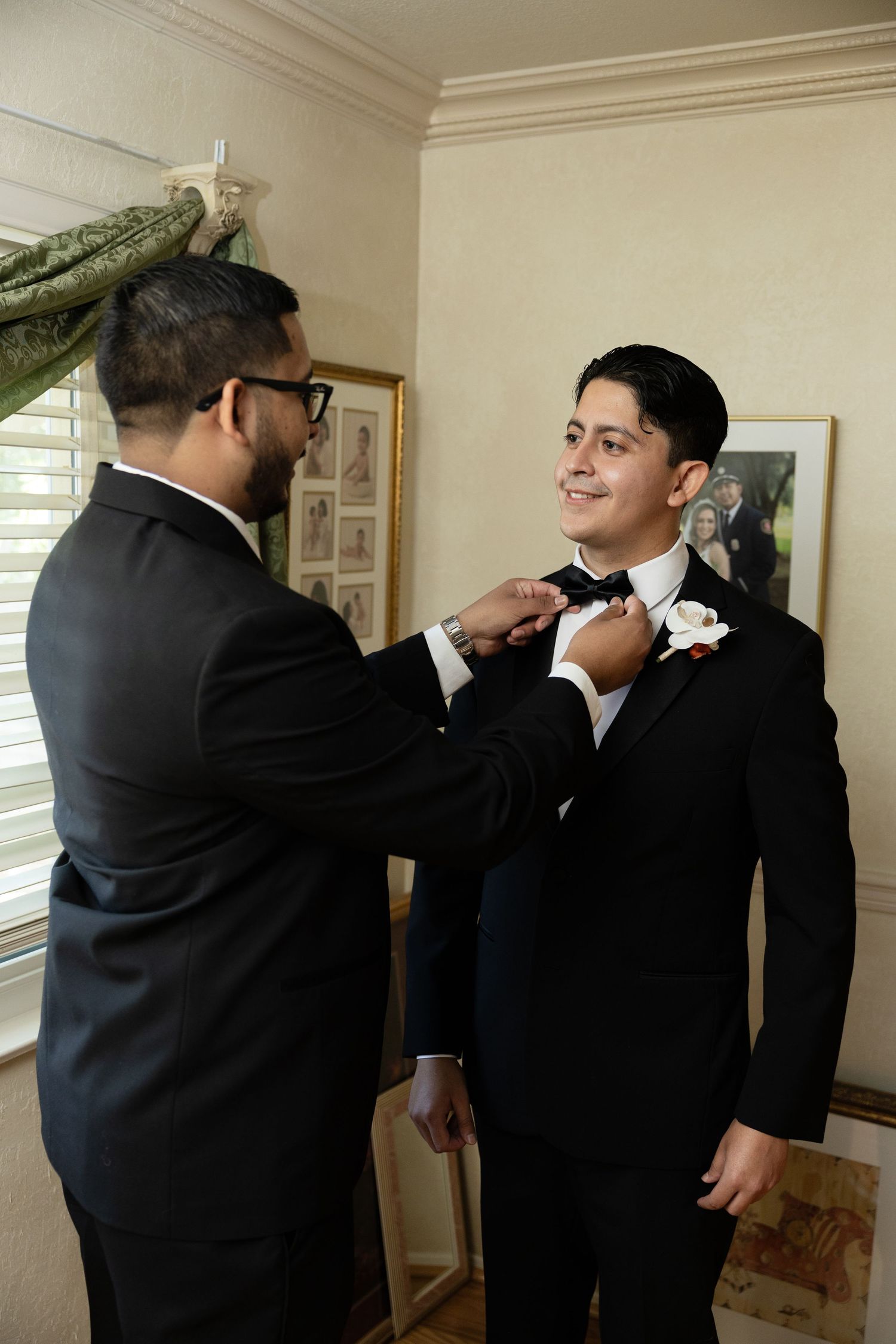 Wedding party members helping adjust a boutonniere on formal attire.