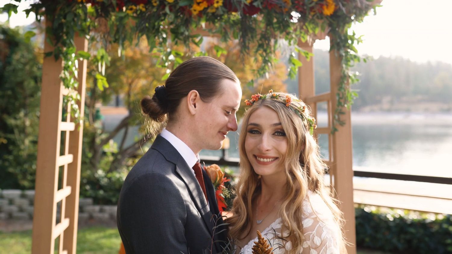 A romantic wedding couple shares intimate moments under autumn trees near a lake.