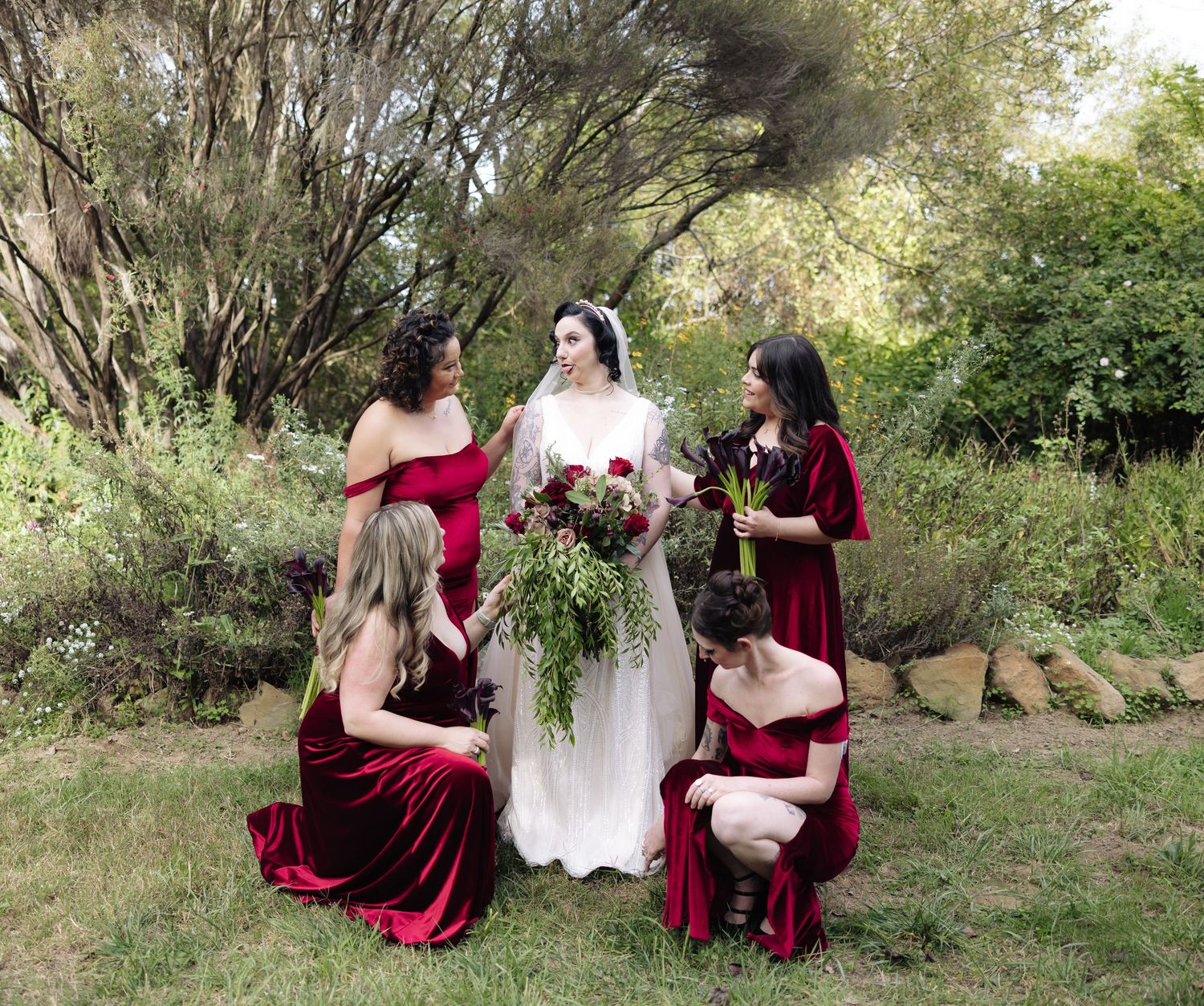Wedding party in burgundy and white poses together on natural outdoor slope.