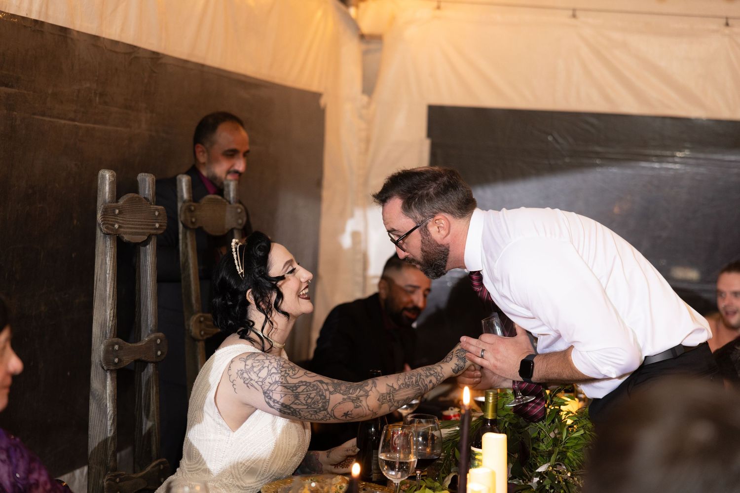 Wedding reception guests enjoying dinner and conversation at elegantly decorated tables with candlelight.