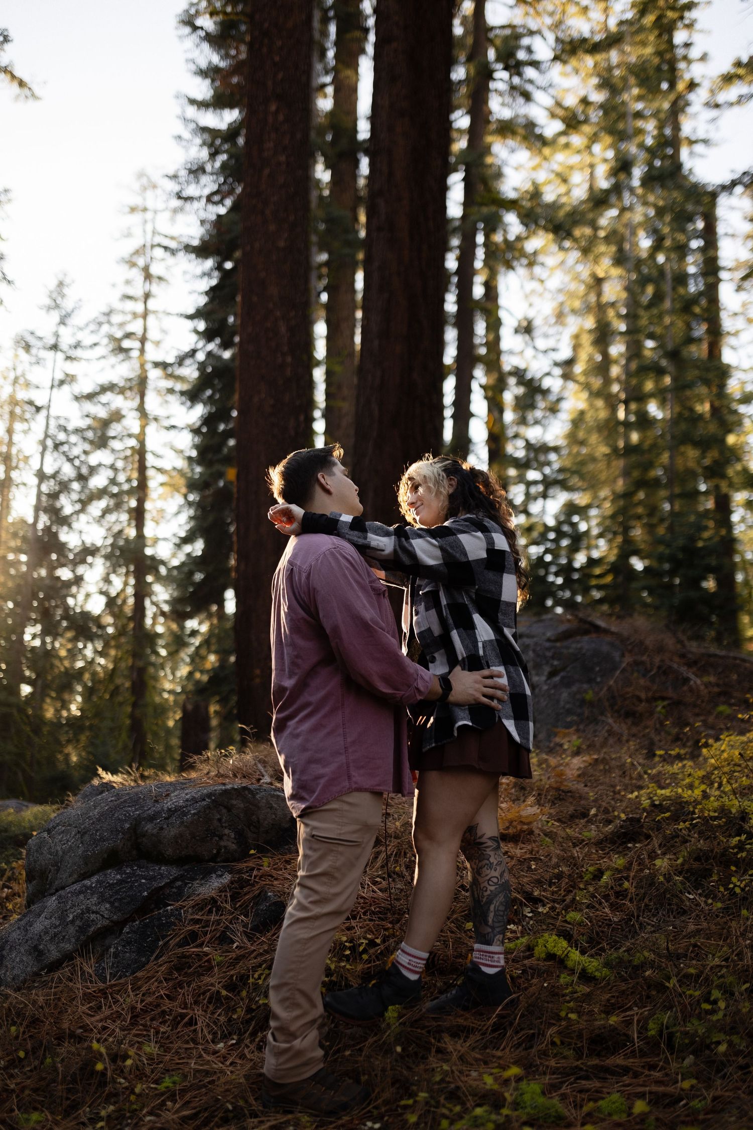Two people embrace while hiking on a rocky forest trail during golden hour.