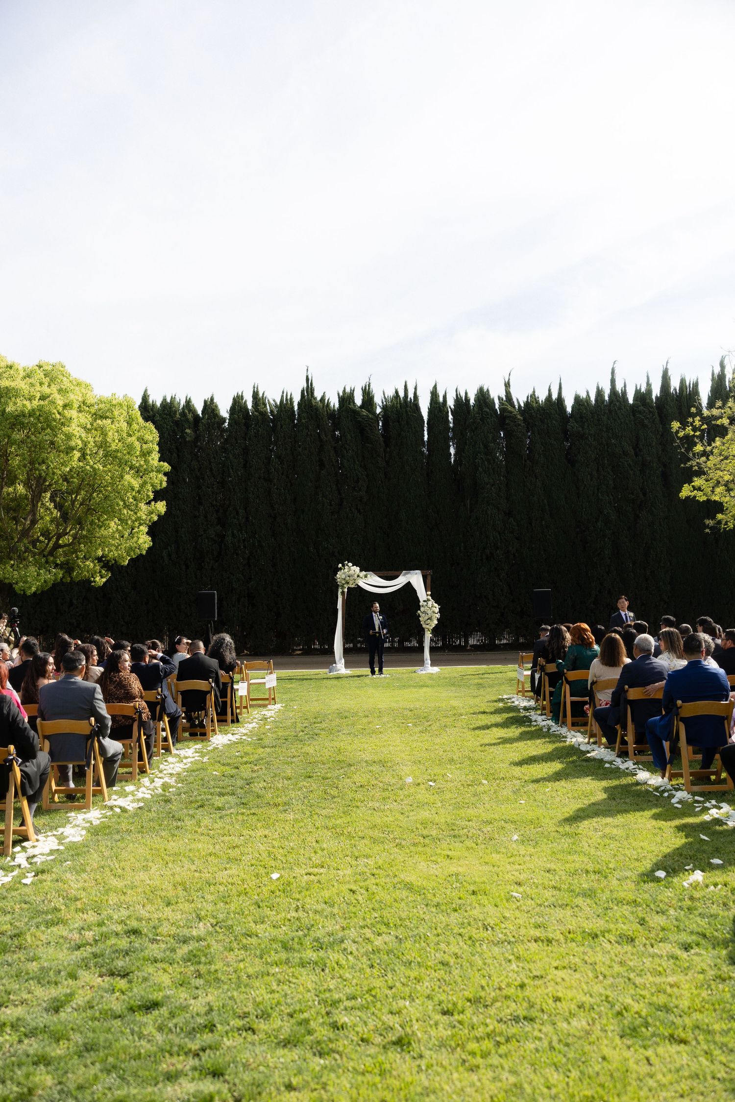Elegant outdoor wedding ceremony on green lawn with floral arch and rows of seated guests.