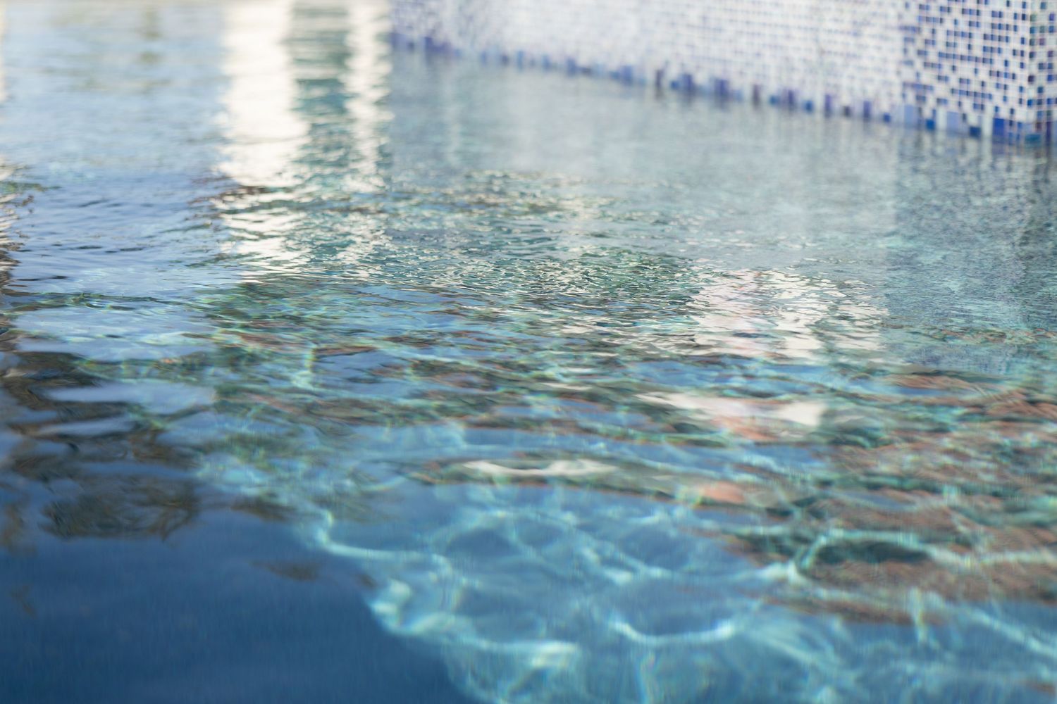 Clear blue rippling water in a swimming pool with sunlight creating shimmering patterns on the surface.