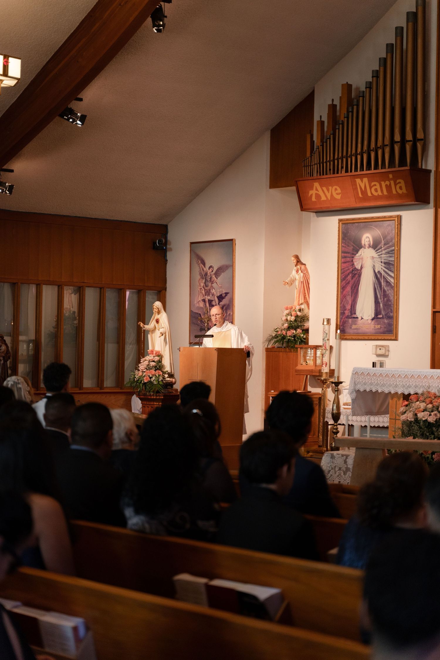 A Catholic church interior during a ceremony with religious artwork and organ pipes visible.