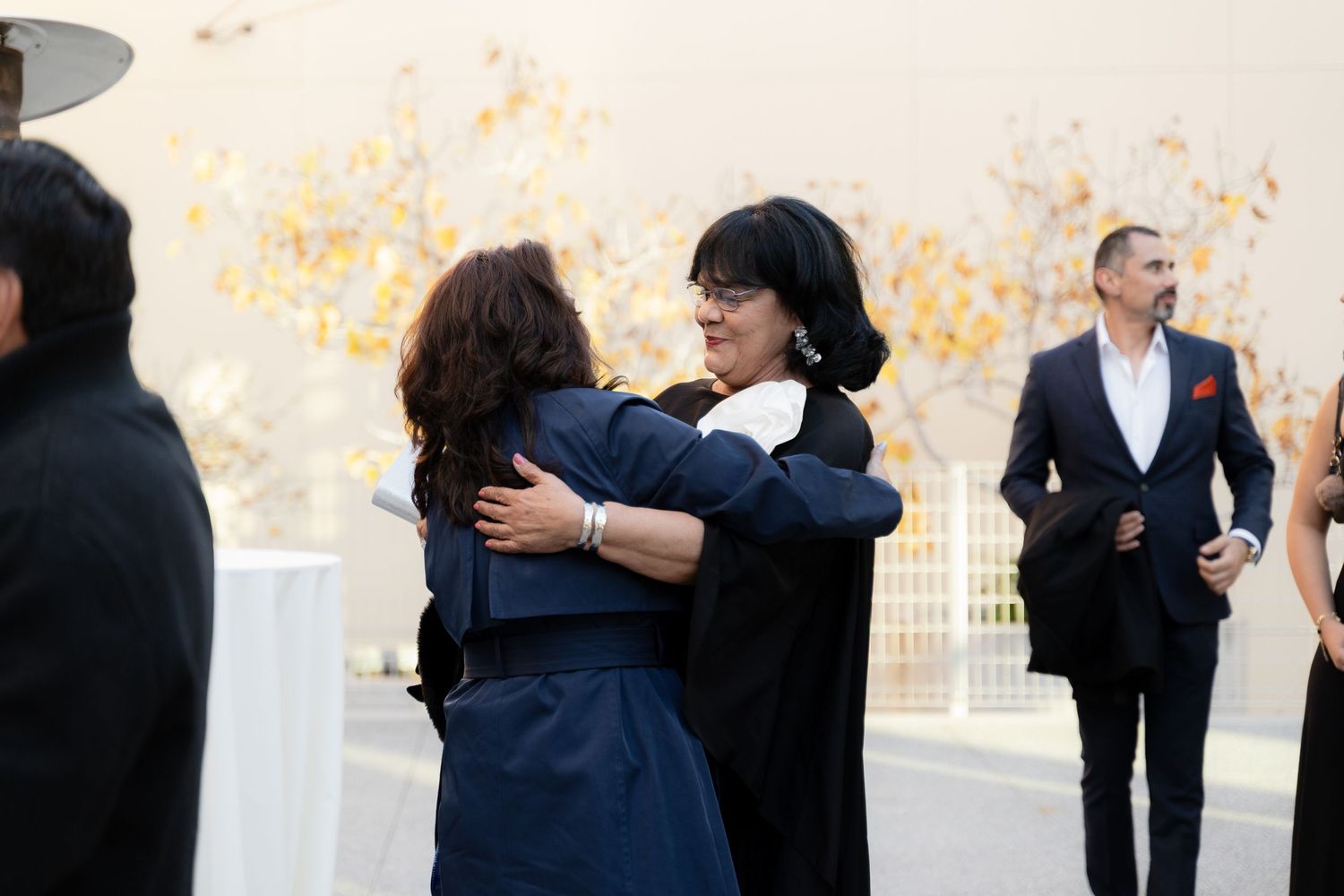 Formal event attendees embrace while others mingle in background.