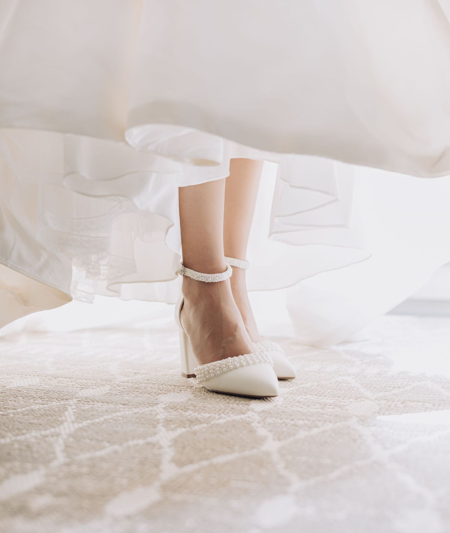 Close-up of delicate white bridal shoes on light colored bedding.