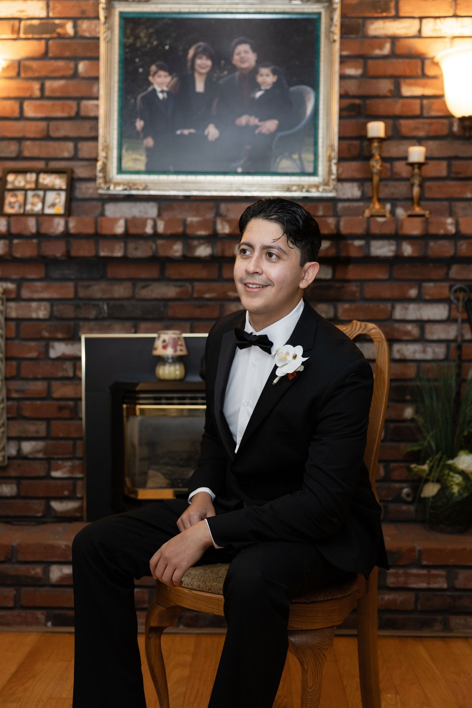 Formal portrait against brick wall showing person in tuxedo seated with warm lighting.