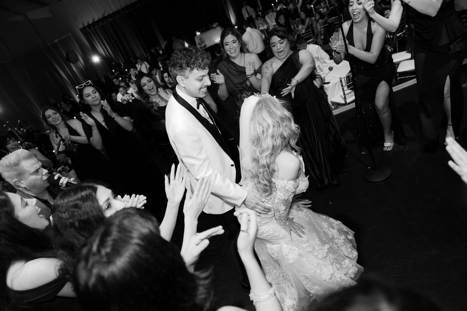 Black and white photo of wedding guests dancing energetically at reception party.