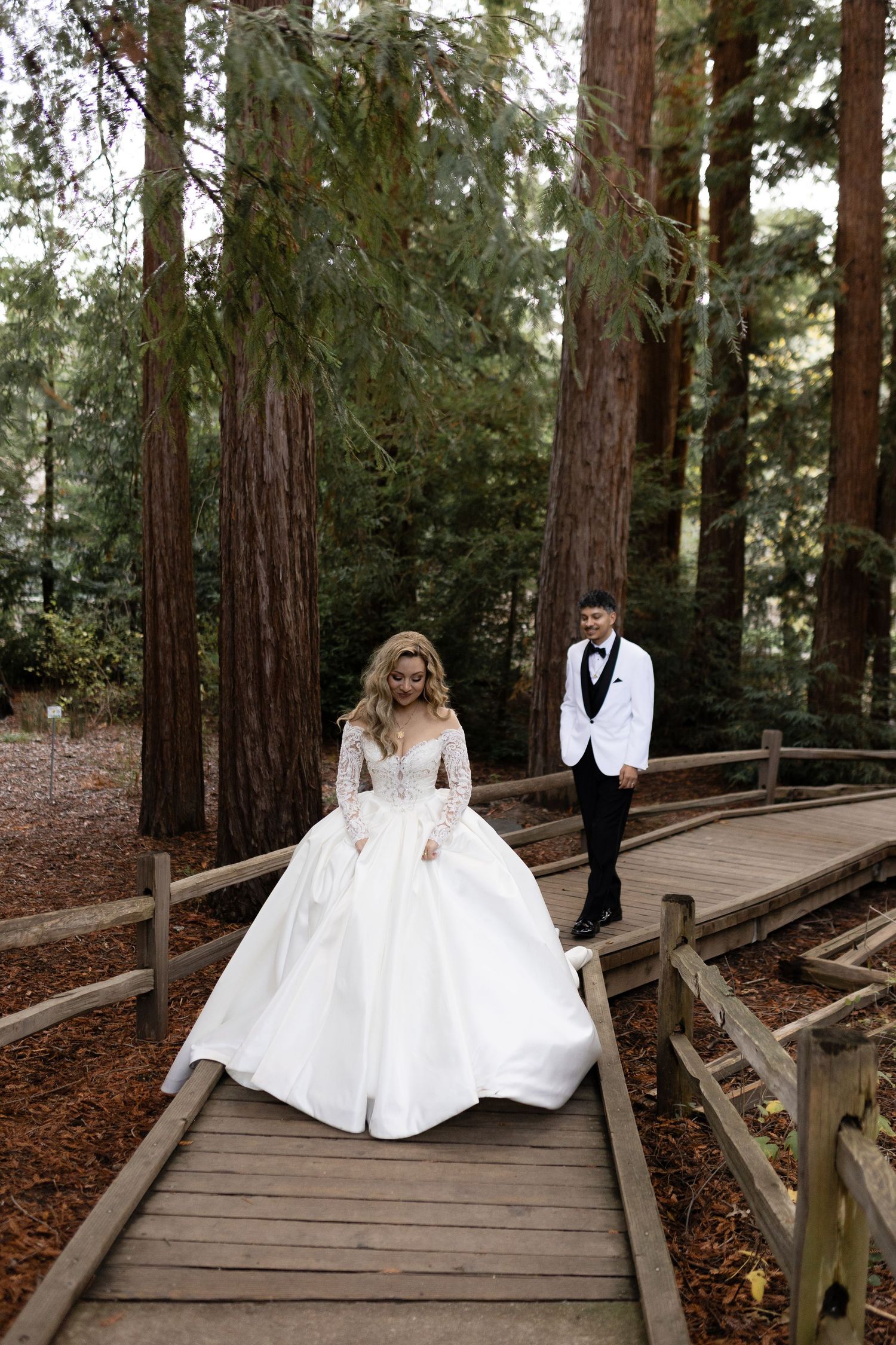 A wedding couple captured in an artistic pose on a wooden walkway through a redwood forest.