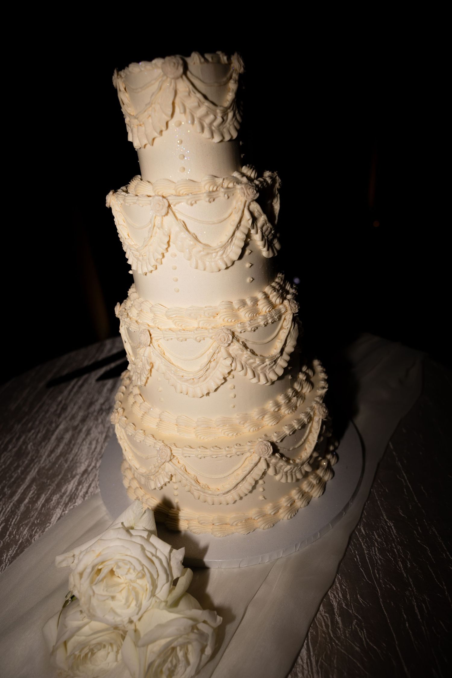 An elegant white tiered wedding cake with delicate piped swag details and roses.