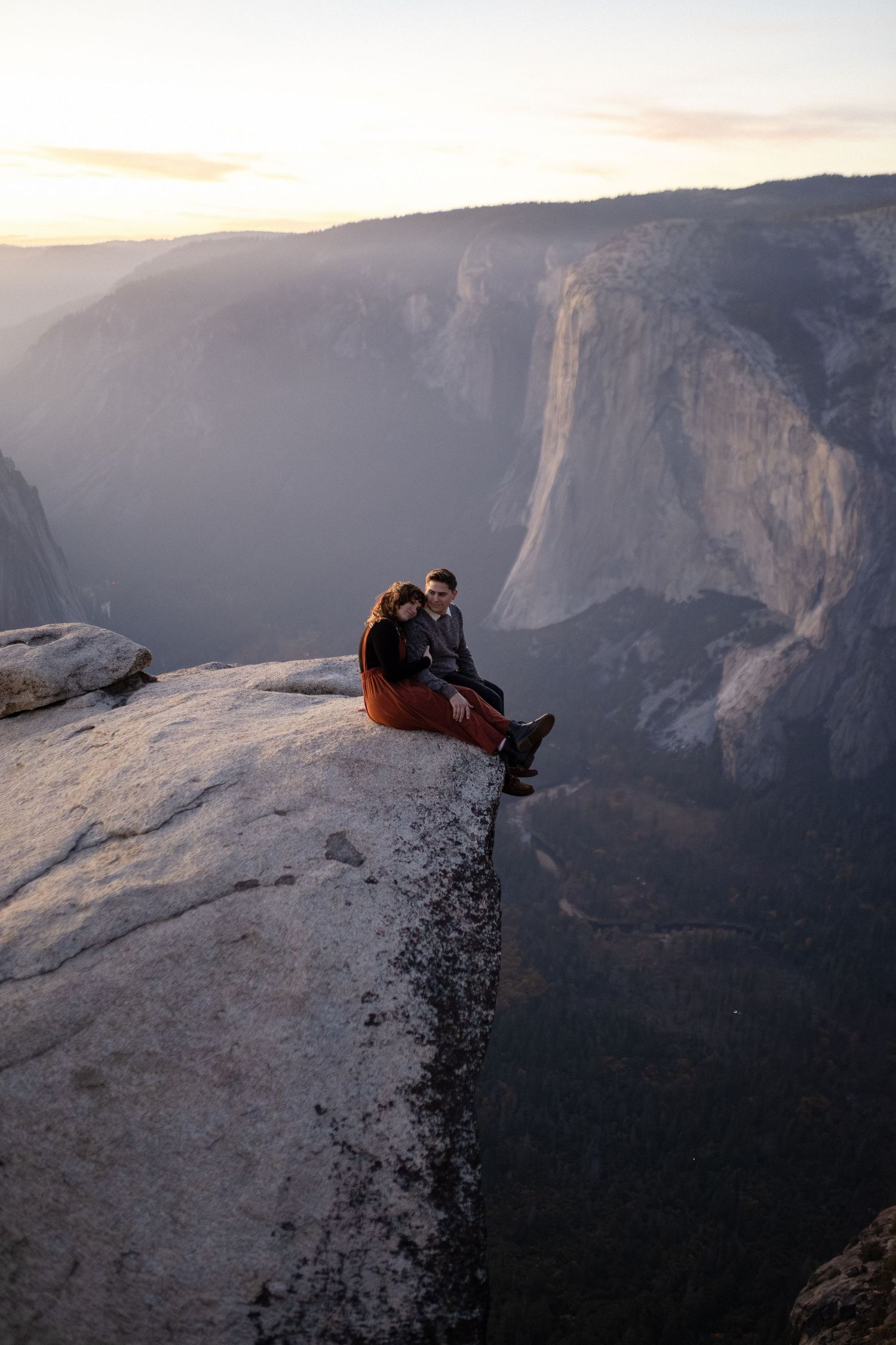 People sitting dangerously close to edge of Taft Point overlooking Yosemite Valley at sunset.