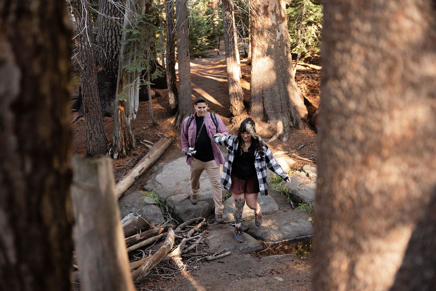 Couple exploring wooded hiking trail surrounded by tall trees.