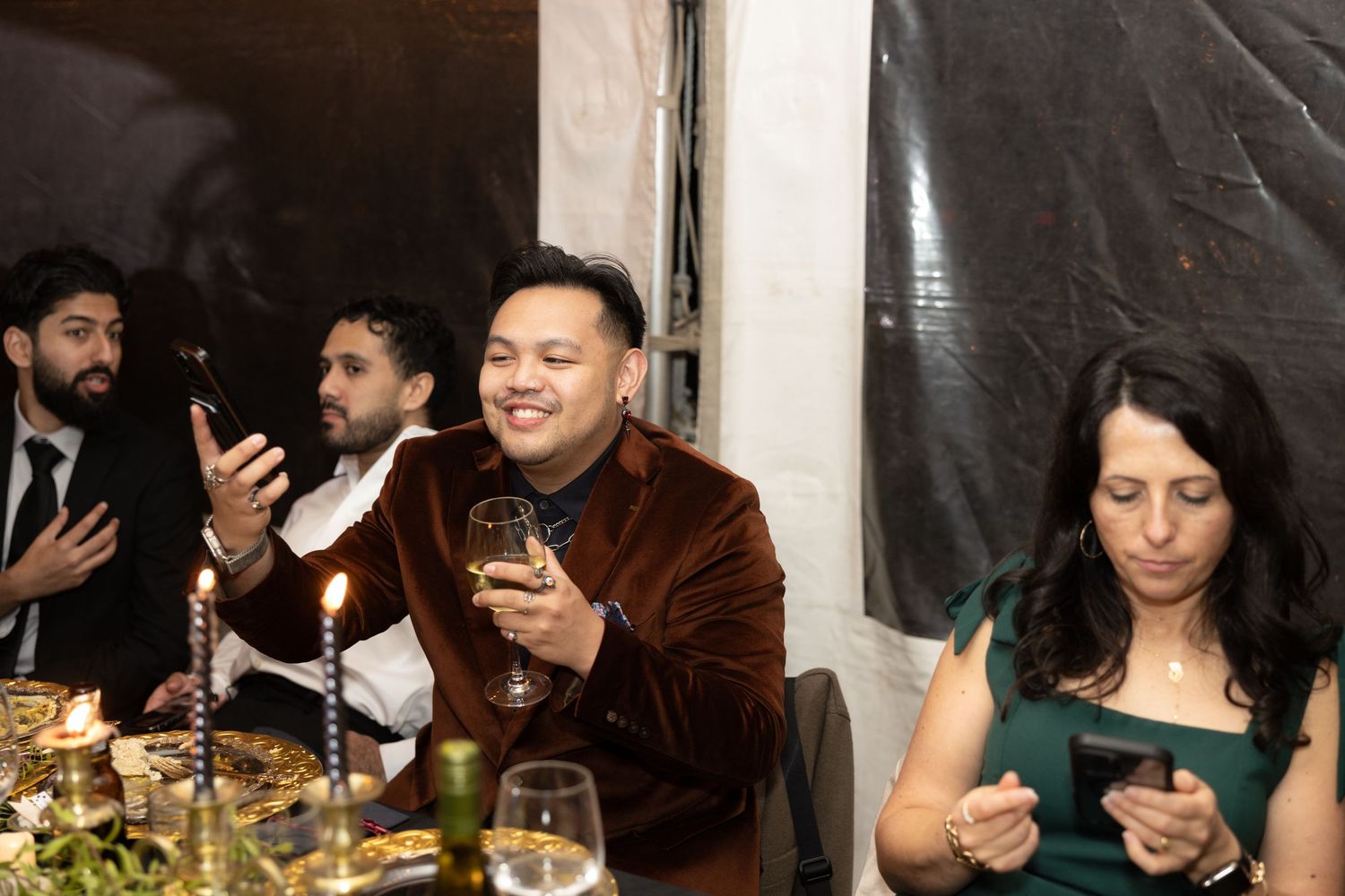 Indoor reception celebration with guests seated at long tables enjoying drinks and conversation.