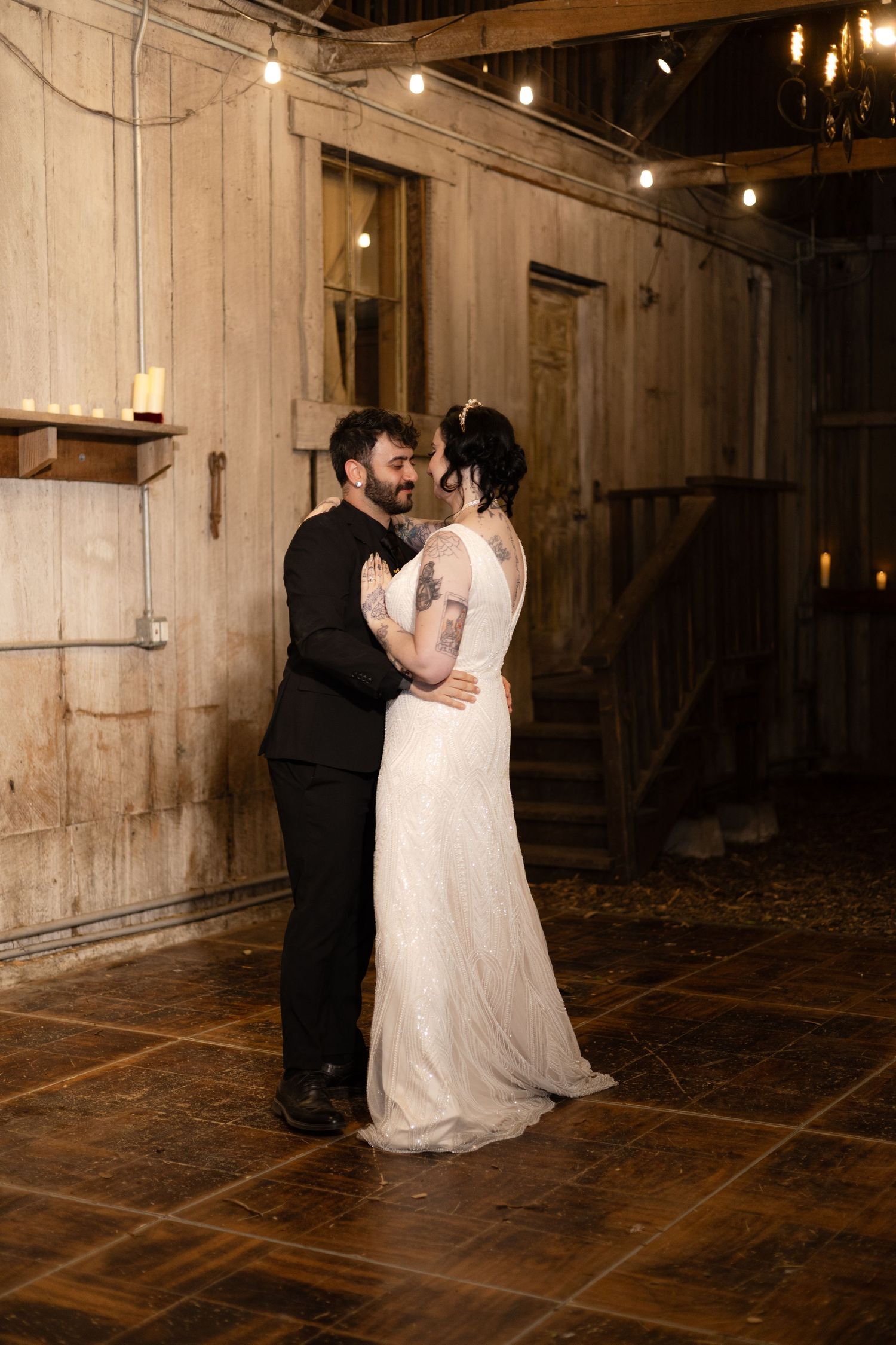 Couple shares a romantic dance moment in a rustic barn with string lights overhead.