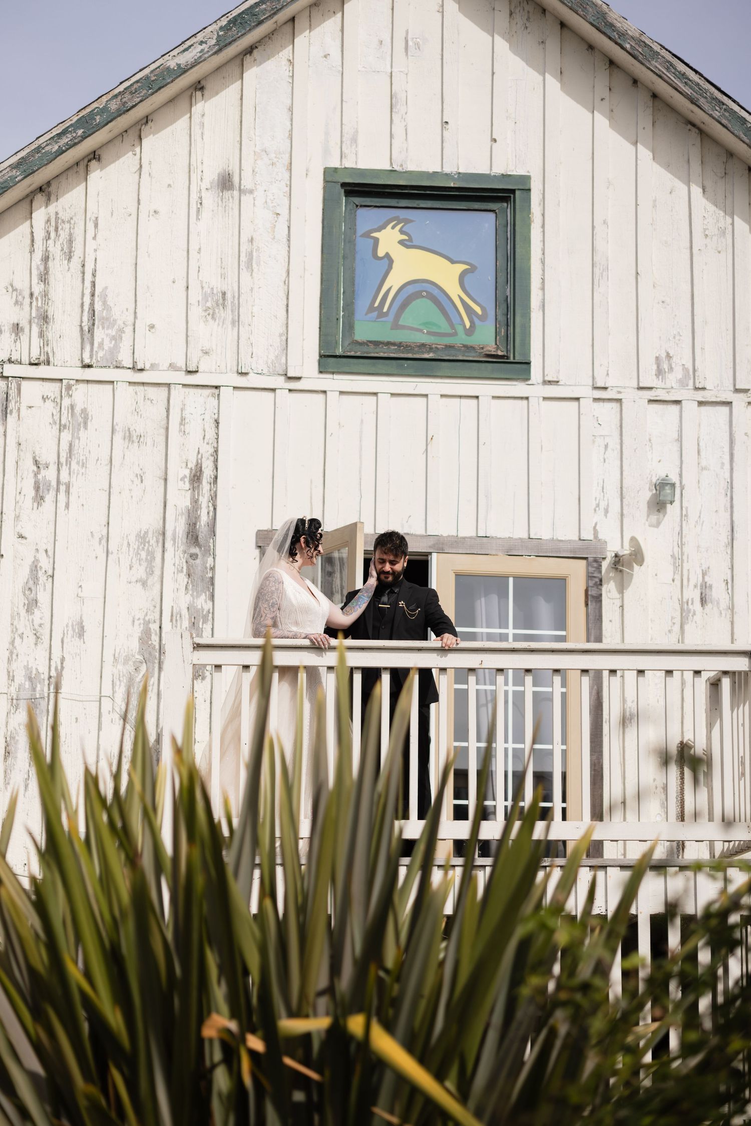 Two figures share an intimate moment on a rustic barn balcony beneath a painted deer emblem.