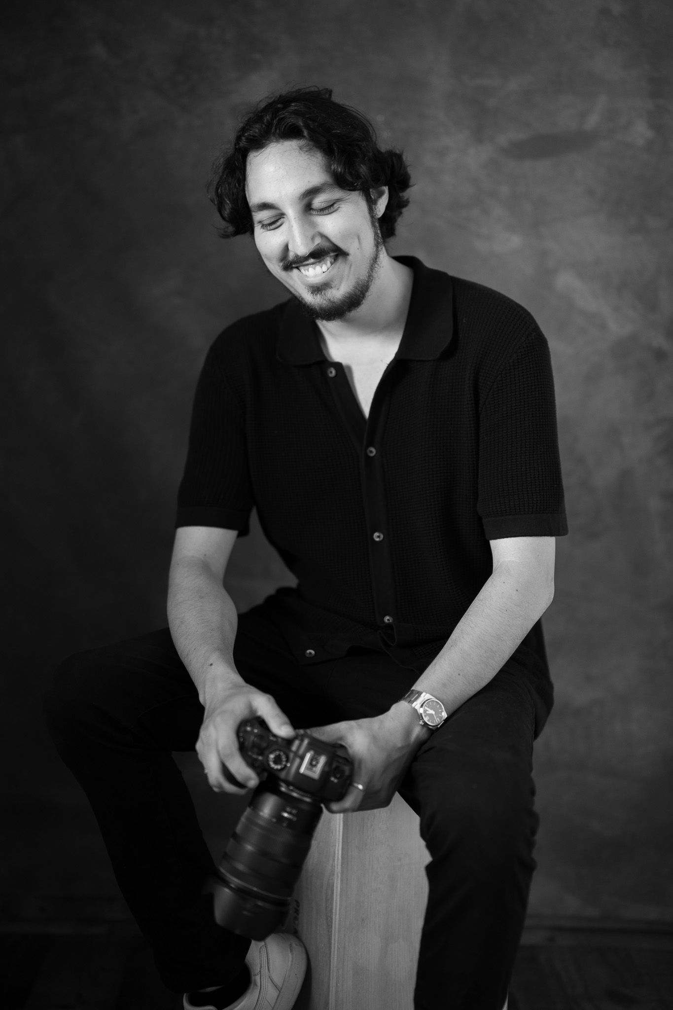 Professional photographer in black attire holding camera in studio setting.