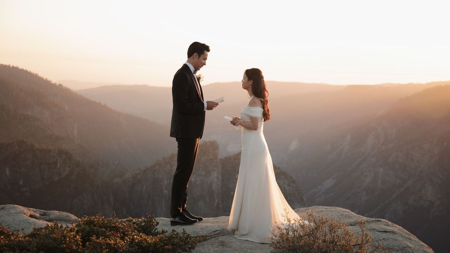 Couple in wedding attire standing on cliff edge at Taft Point during golden hour.