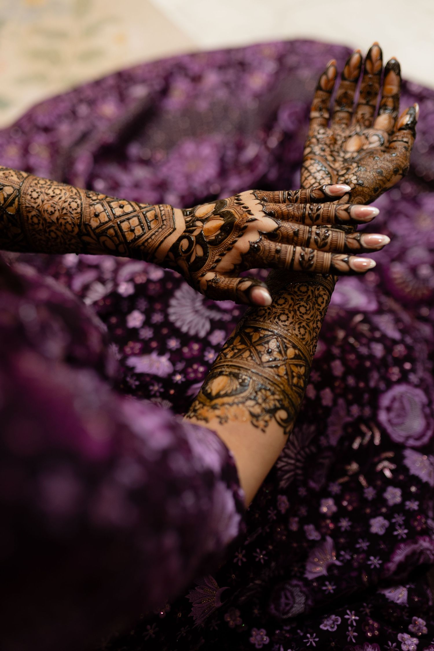 Intricate henna designs adorning hands with delicate patterns against a purple bokeh background.