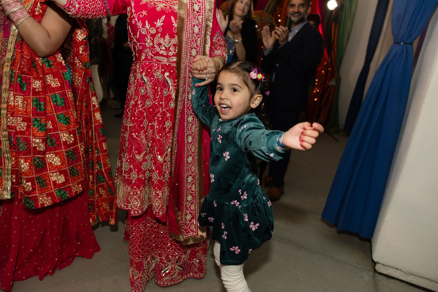 A group of people in traditional red and green outfits gather at a festive celebration with decorative lighting.