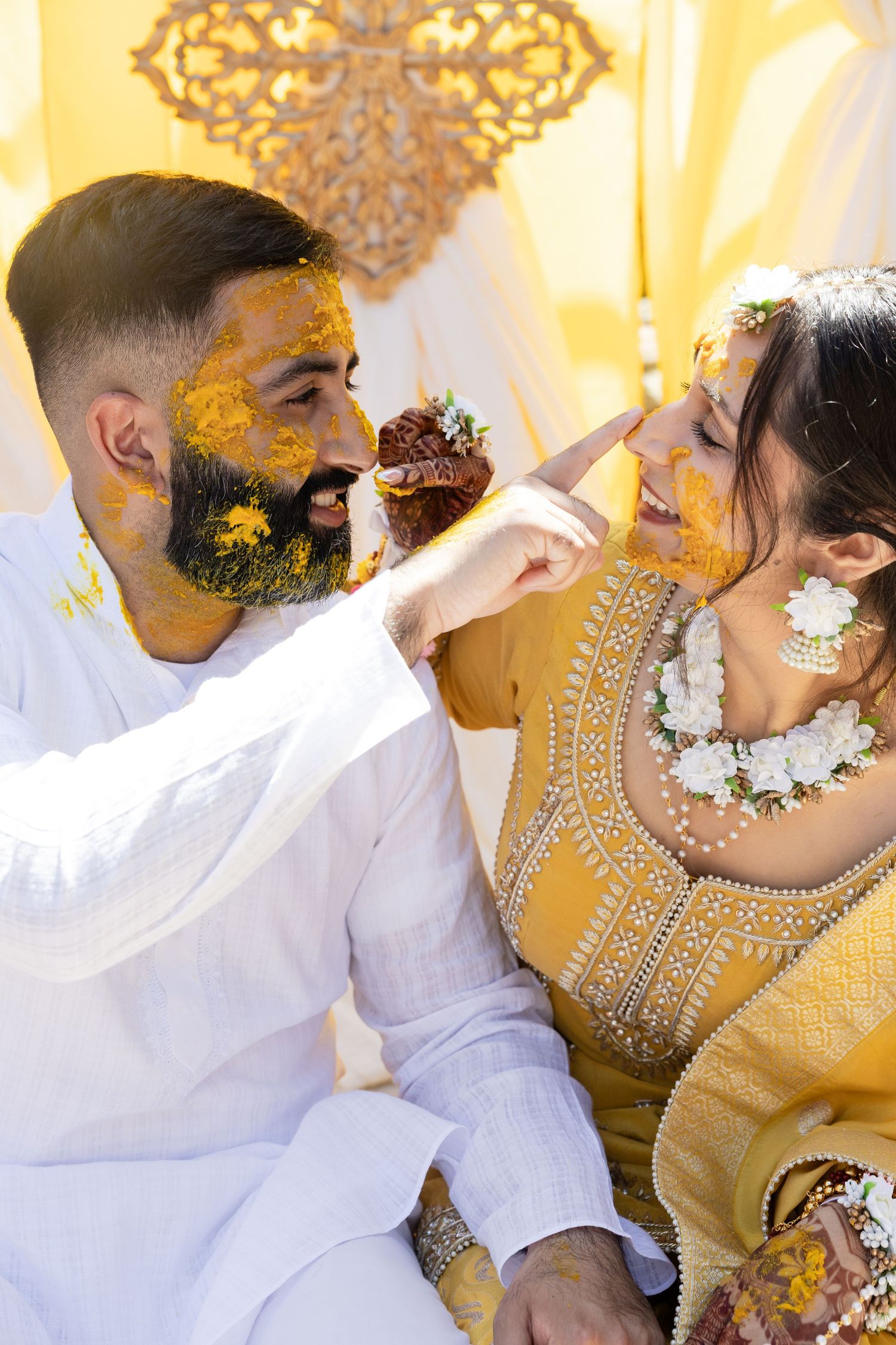 Wedding couple in traditional yellow and white attire share intimate moments against ornate golden backdrop.