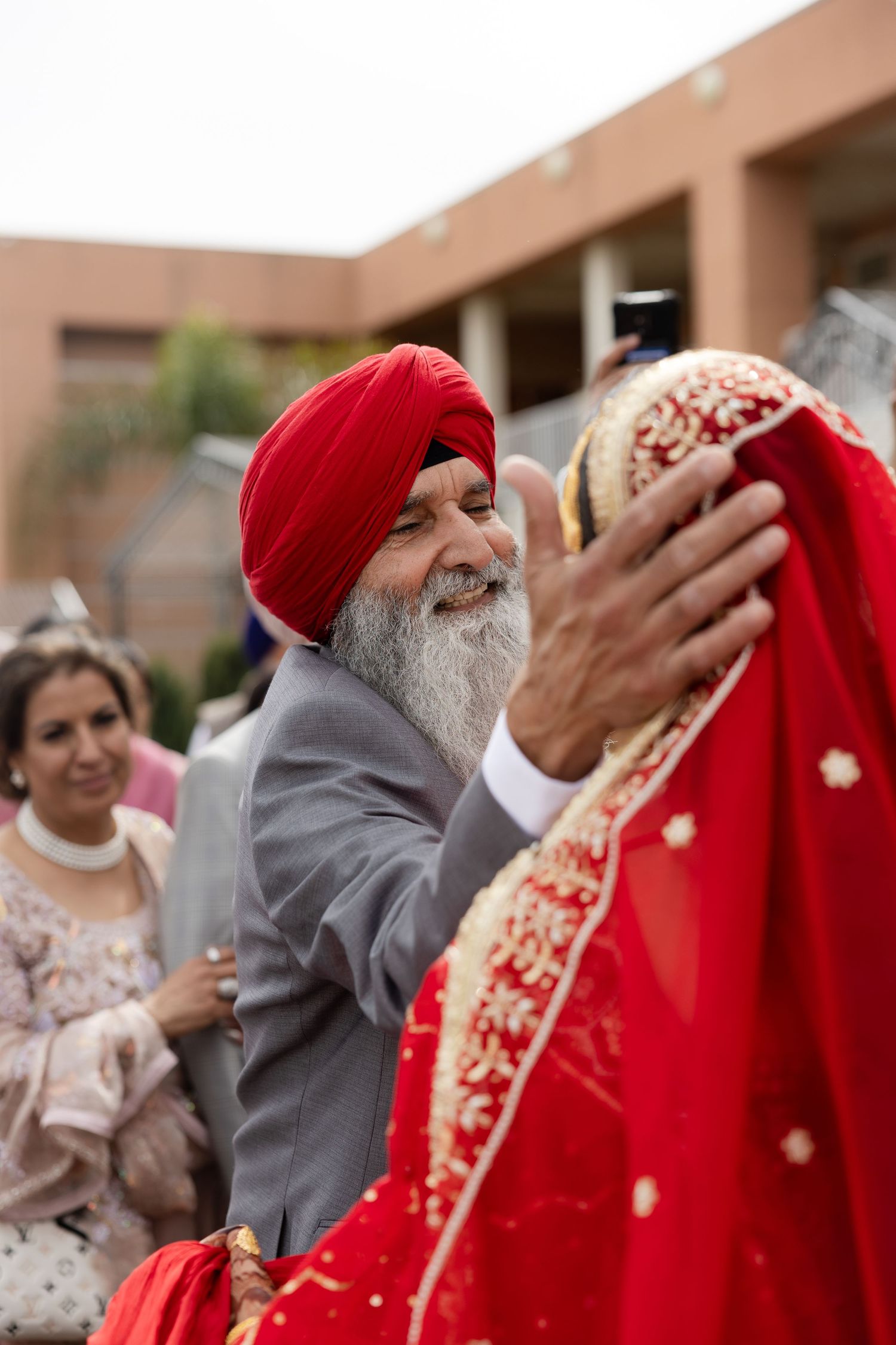 Wedding guests celebrate during a traditional Sikh ceremony with bright red attire and festive expressions.