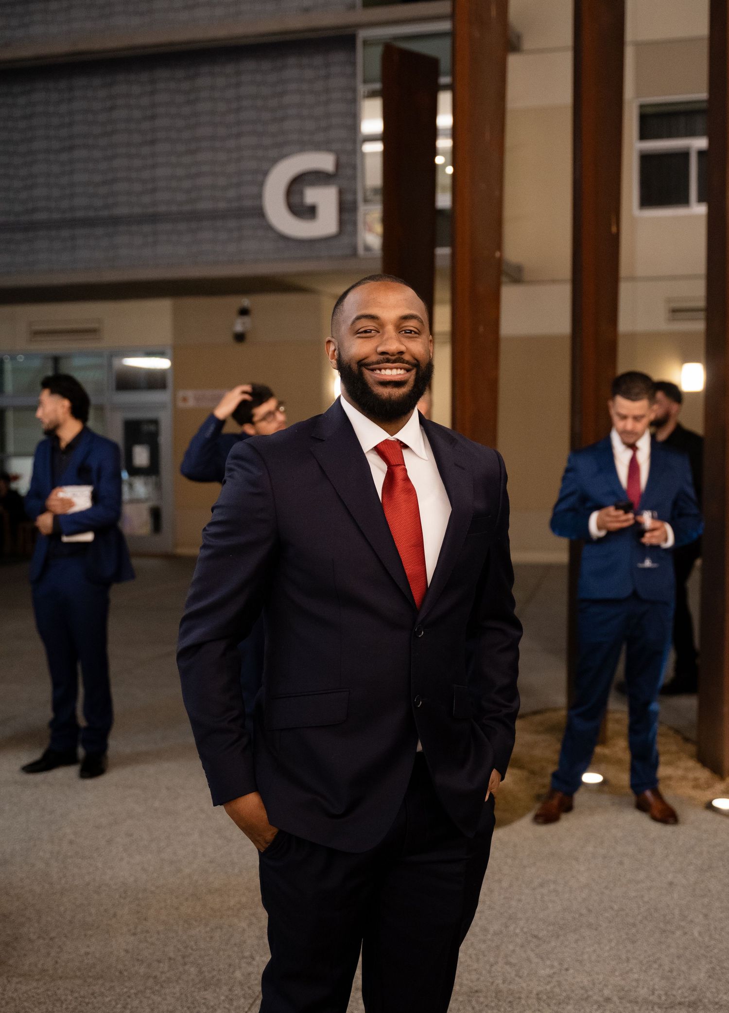 Groomsmen in dark suits and red ties pose together at a wedding venue.