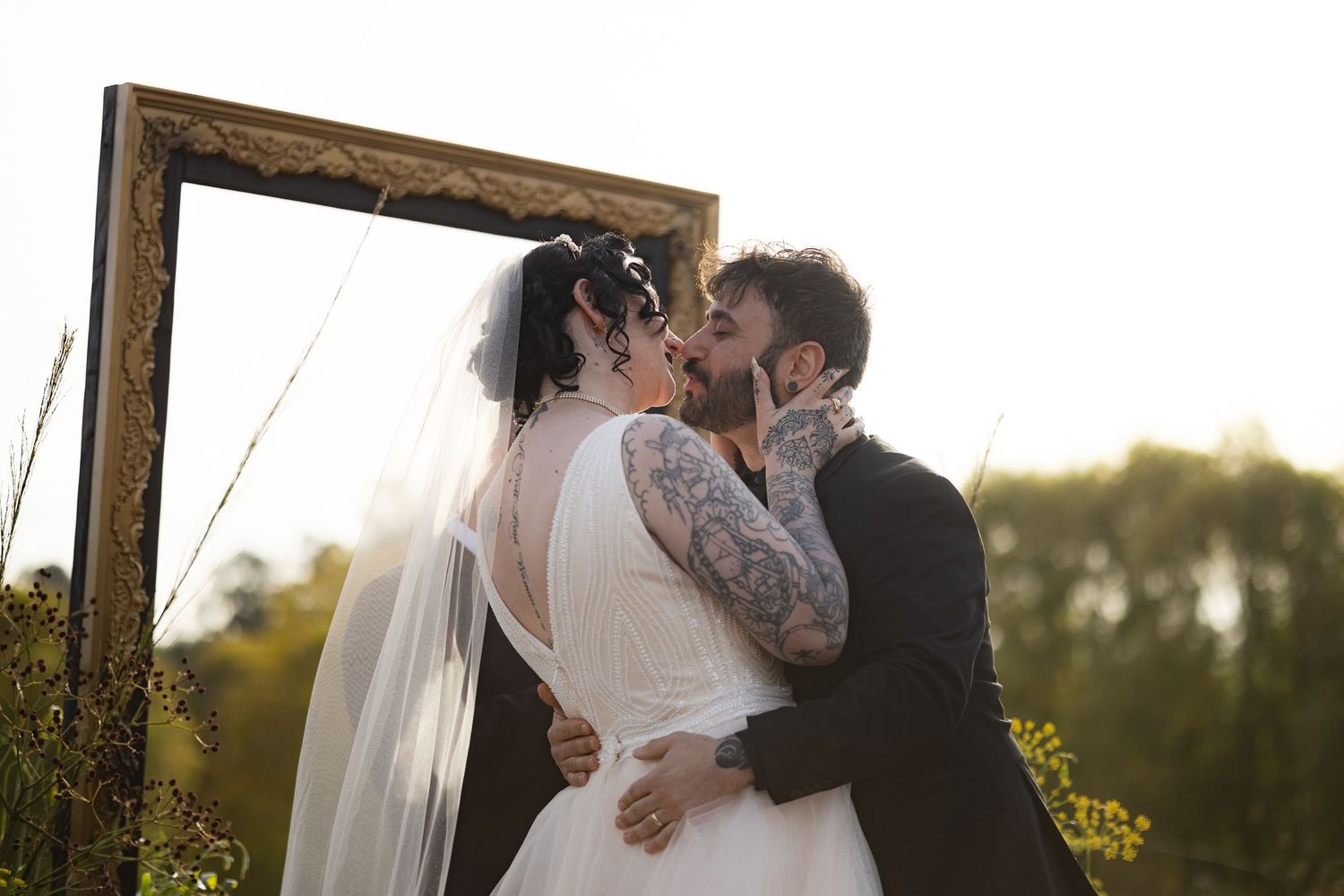 Newlyweds share a romantic moment under wooden arch during sunset wedding ceremony.
