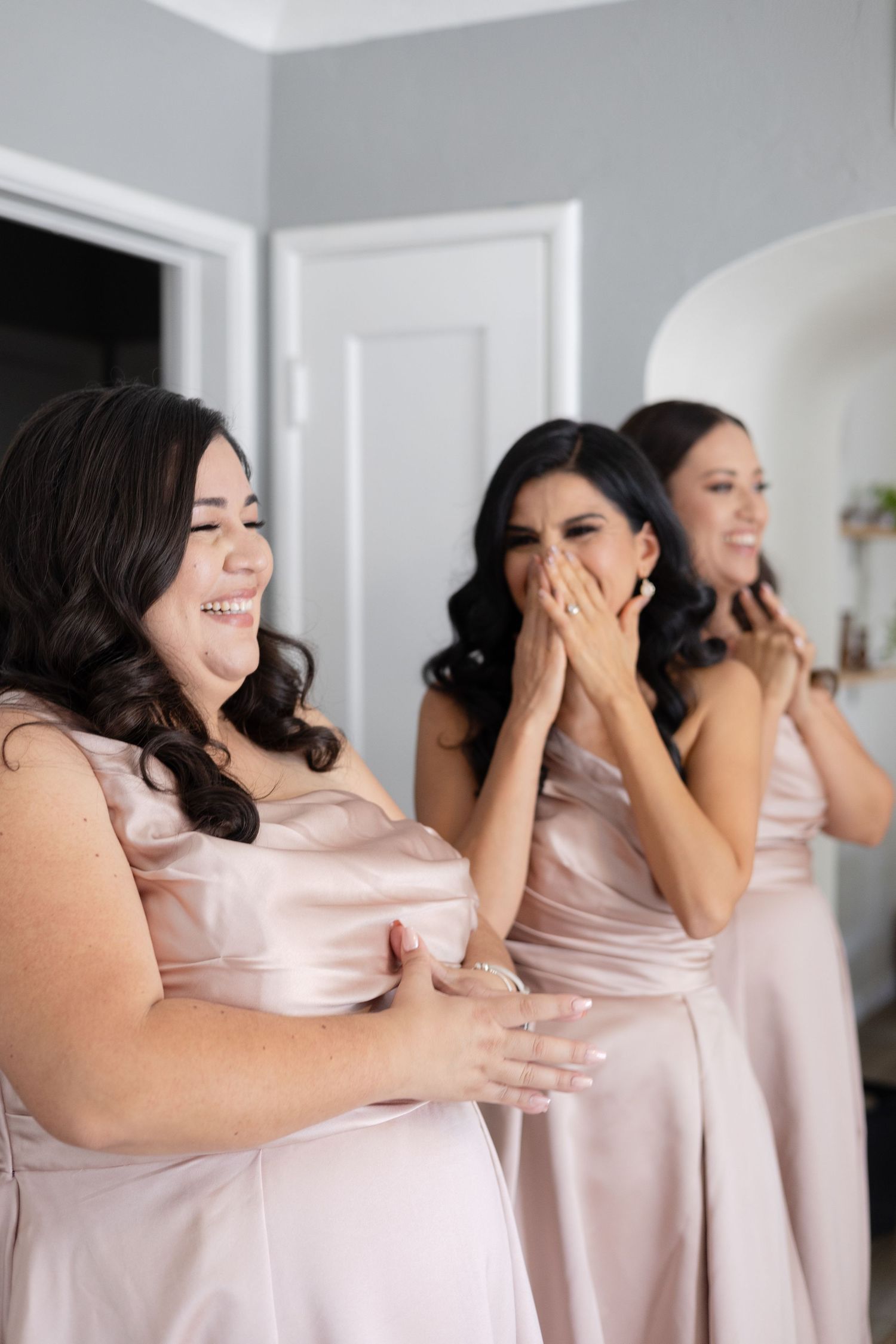 Three bridesmaids share an emotional moment of laughter while wearing matching pink gowns.