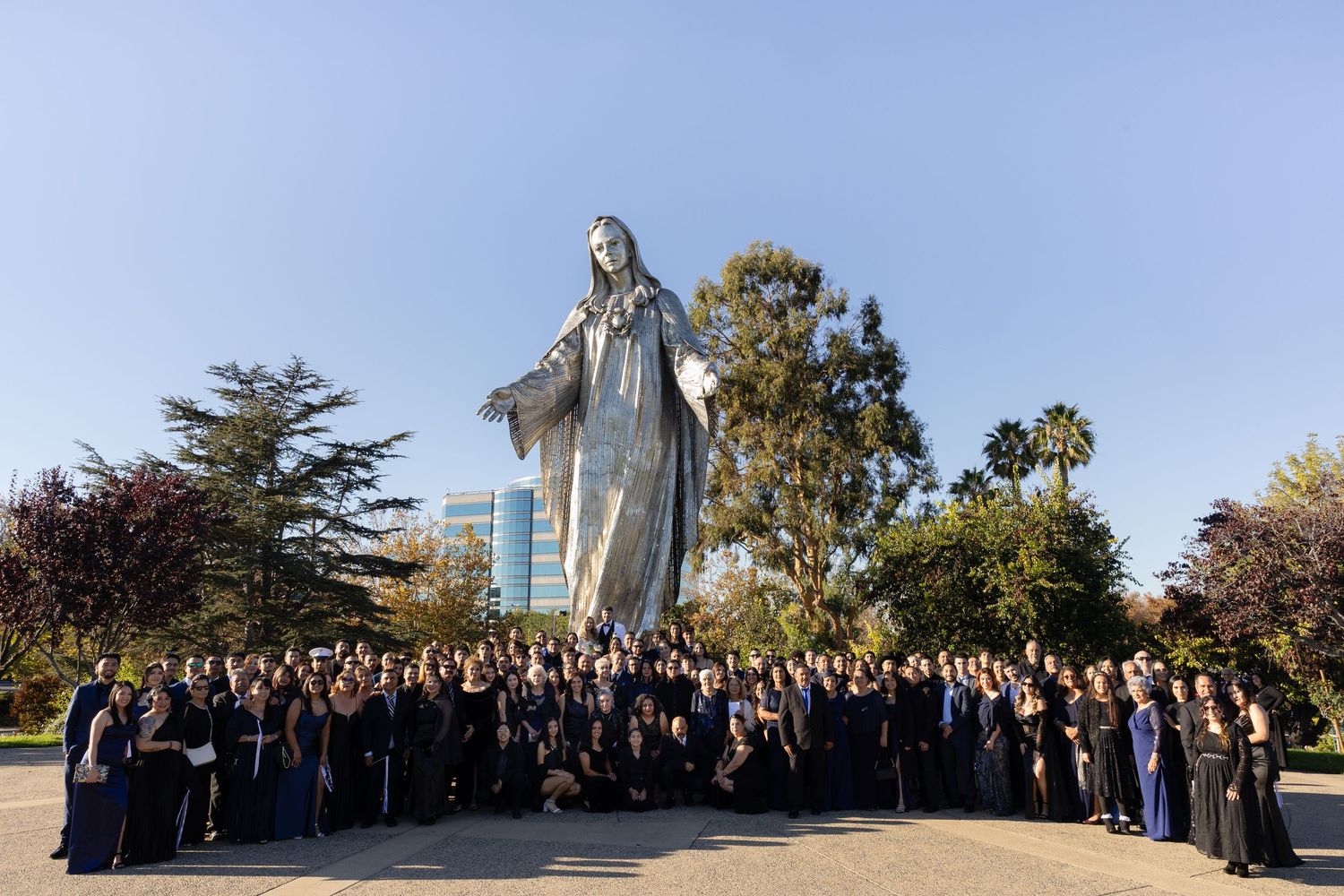 Large wedding group poses for a panoramic photo on a sunny afternoon.