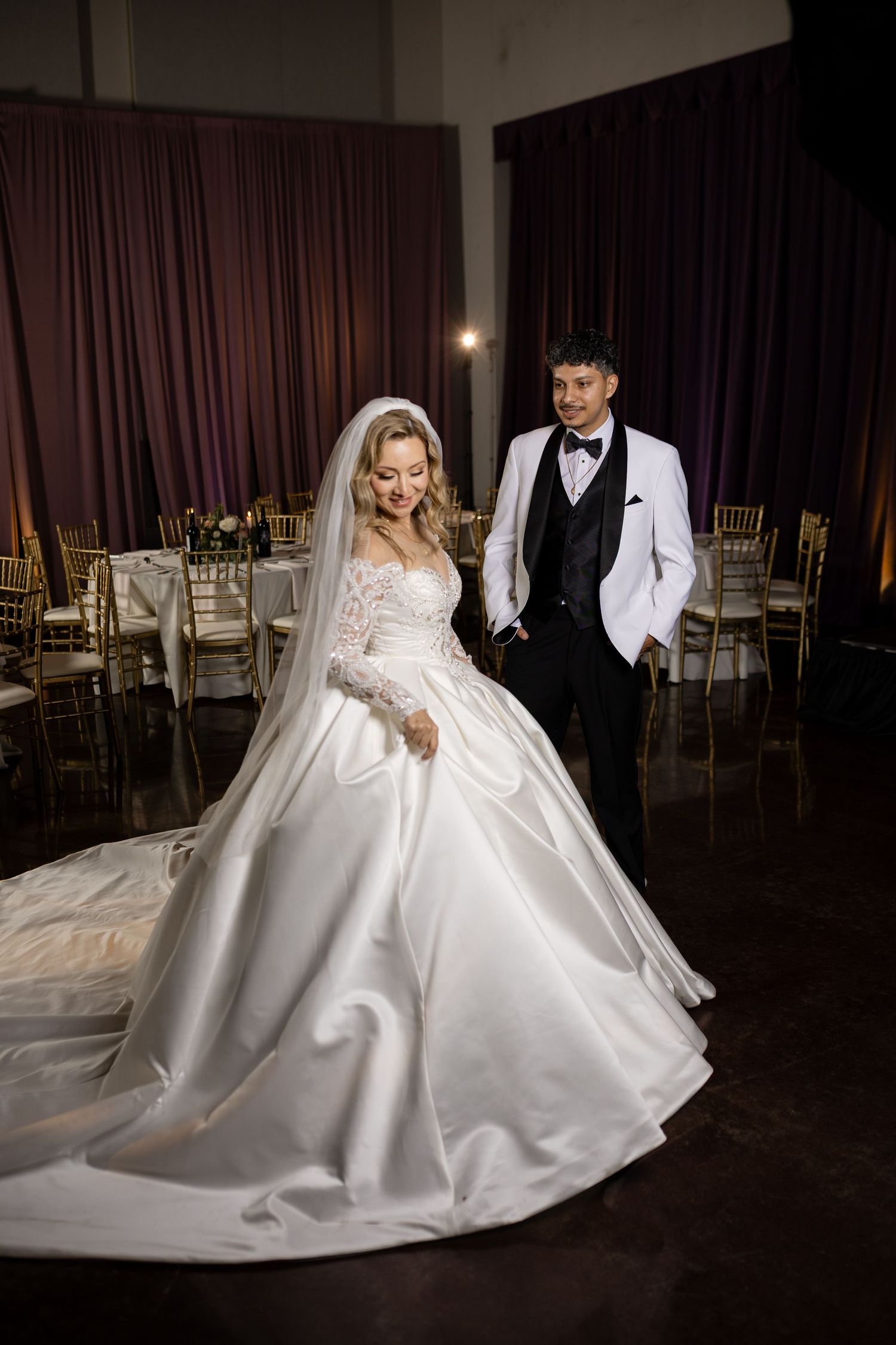 A glamorous wedding couple creates artistic silhouettes against dramatic ballroom lighting.